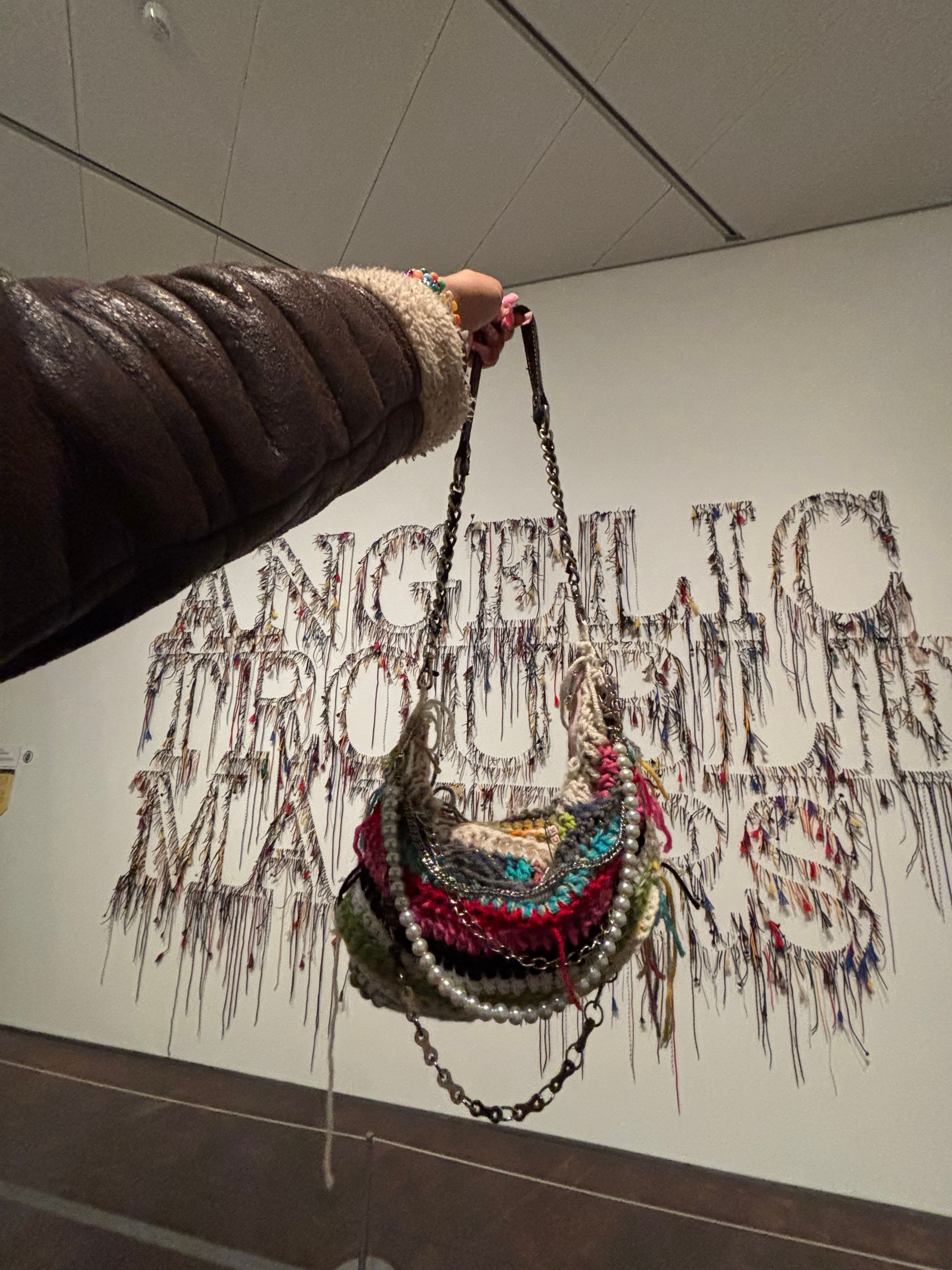 Person holding a beaded bag with a dragon design, standing in front of a wall with graffiti-style art.