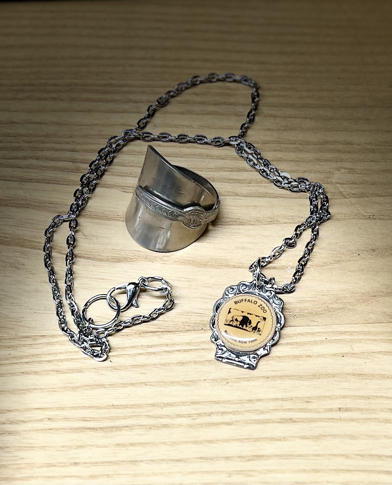 A silver ring and a chain with a round pendant on a wooden surface.
