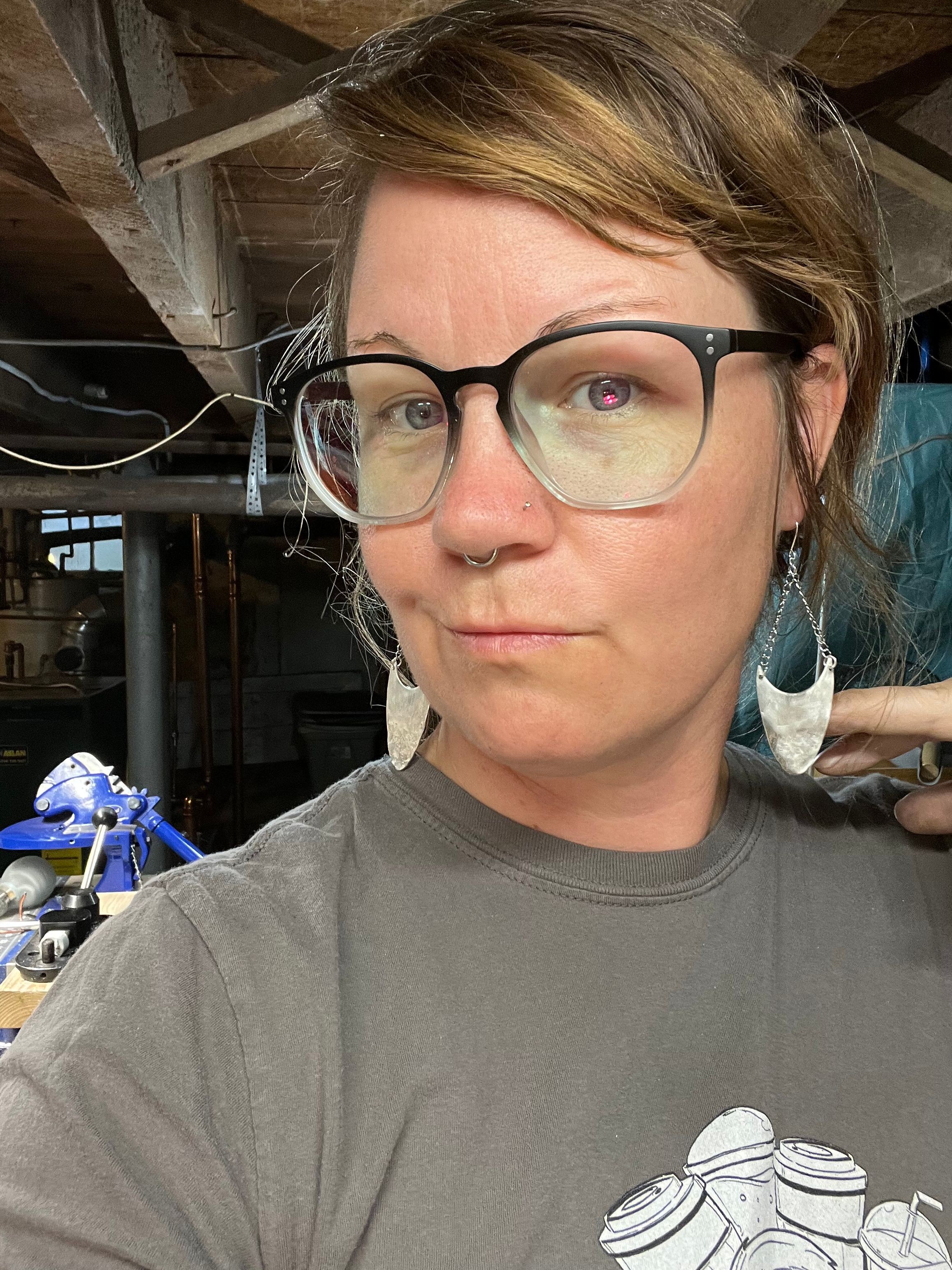 Person with glasses and headphones, looking at the camera, in an indoor setting with various objects in the background.