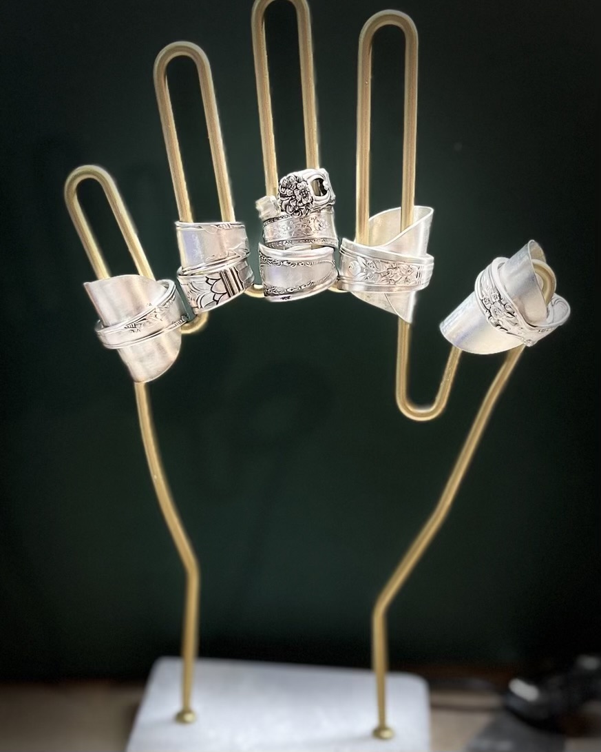 Metal hand-shaped jewelry display with rings and earrings, set against a dark background.