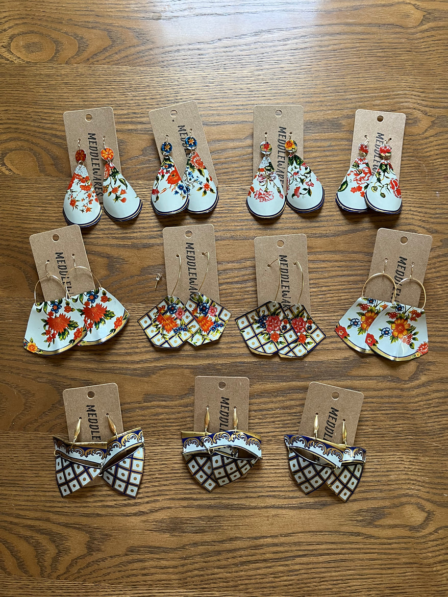 Four pairs of Christmas-themed earrings with snowmen, ornaments, and gift designs, arranged on a wooden surface.