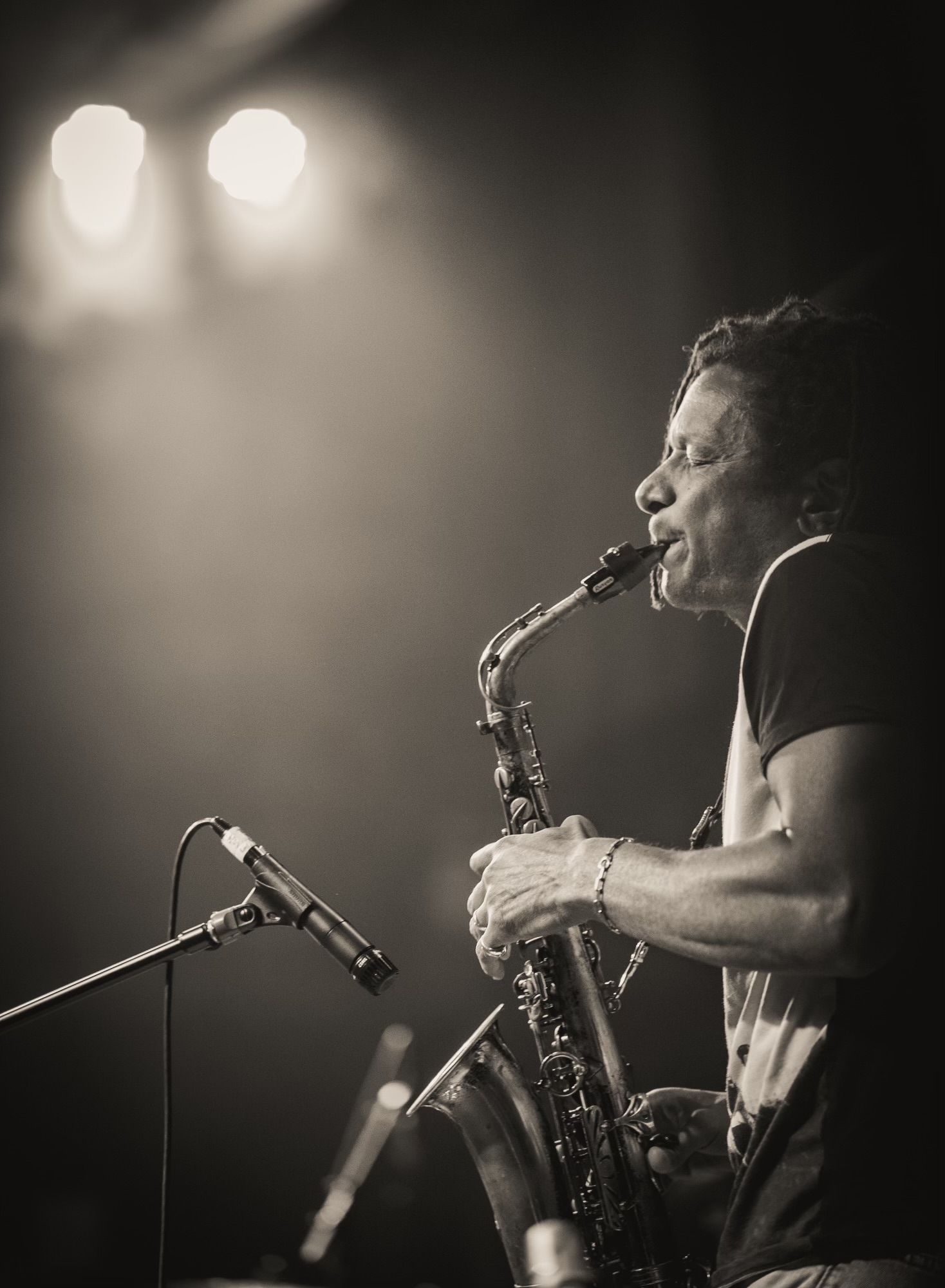 A person playing a saxophone on stage with bright lights behind them, in black and white.