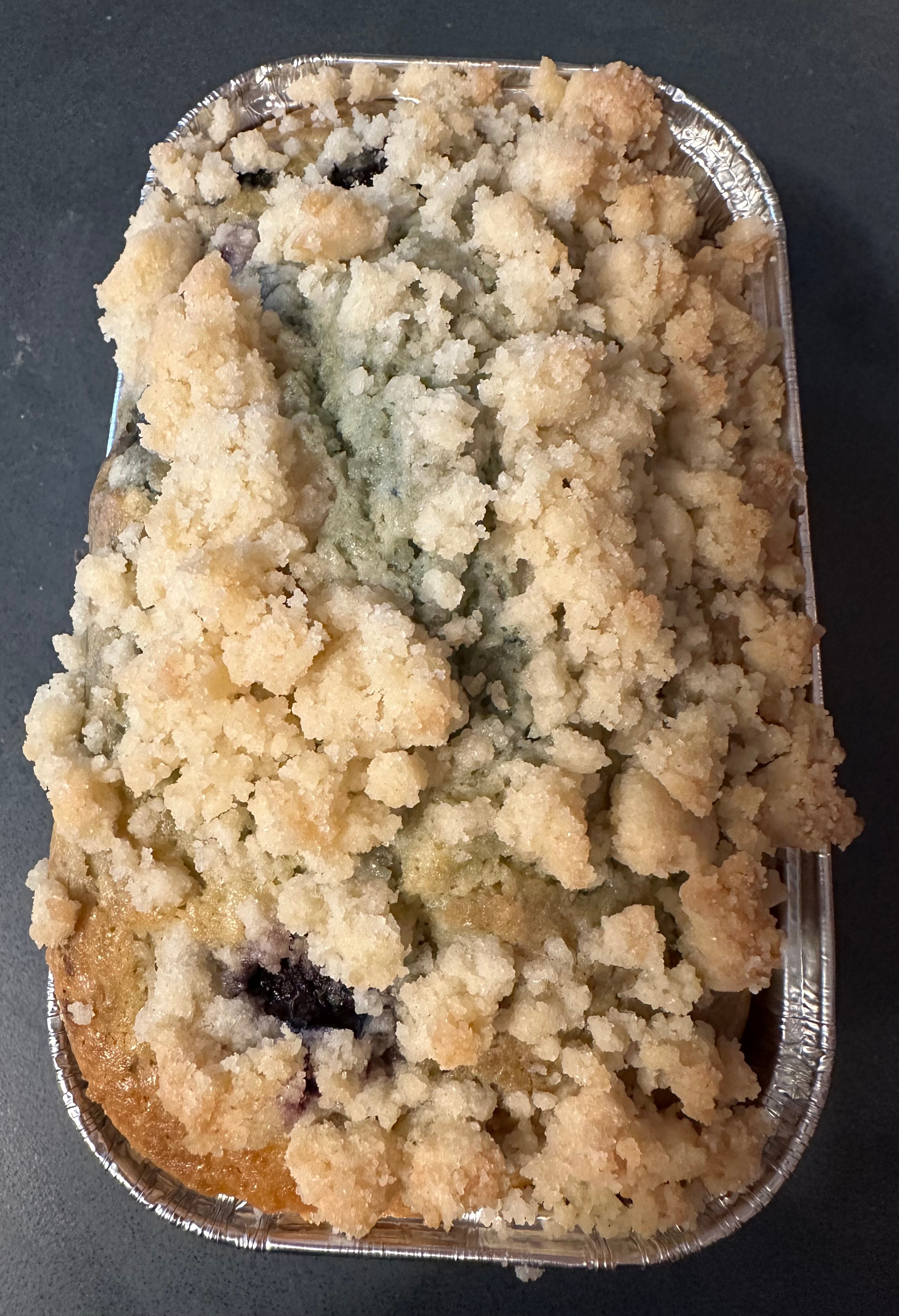 Crumbly baked dish in a metal container with a dark background.