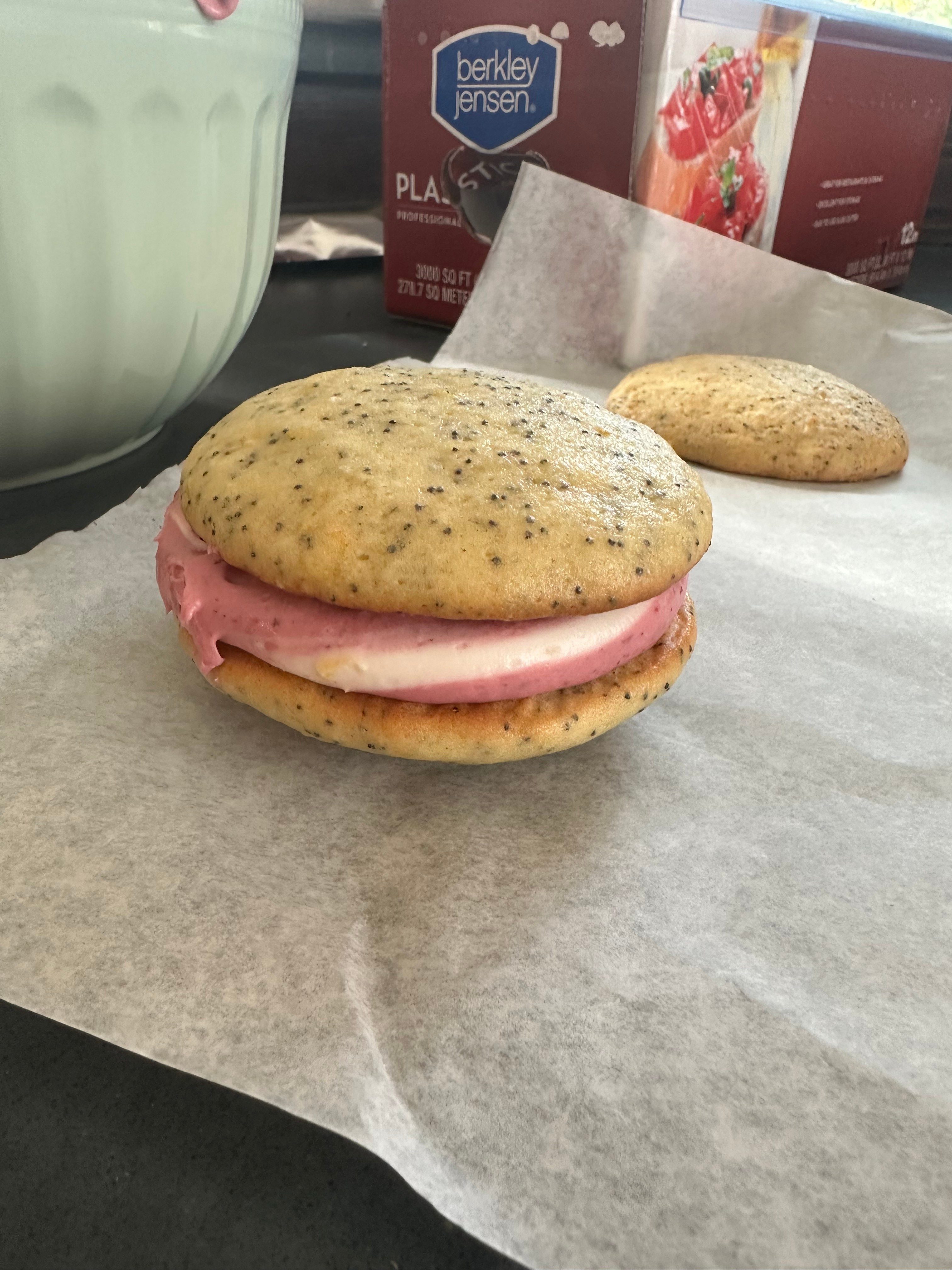 Sandwich with pink meat and bread on parchment paper, with a cookie in the background.