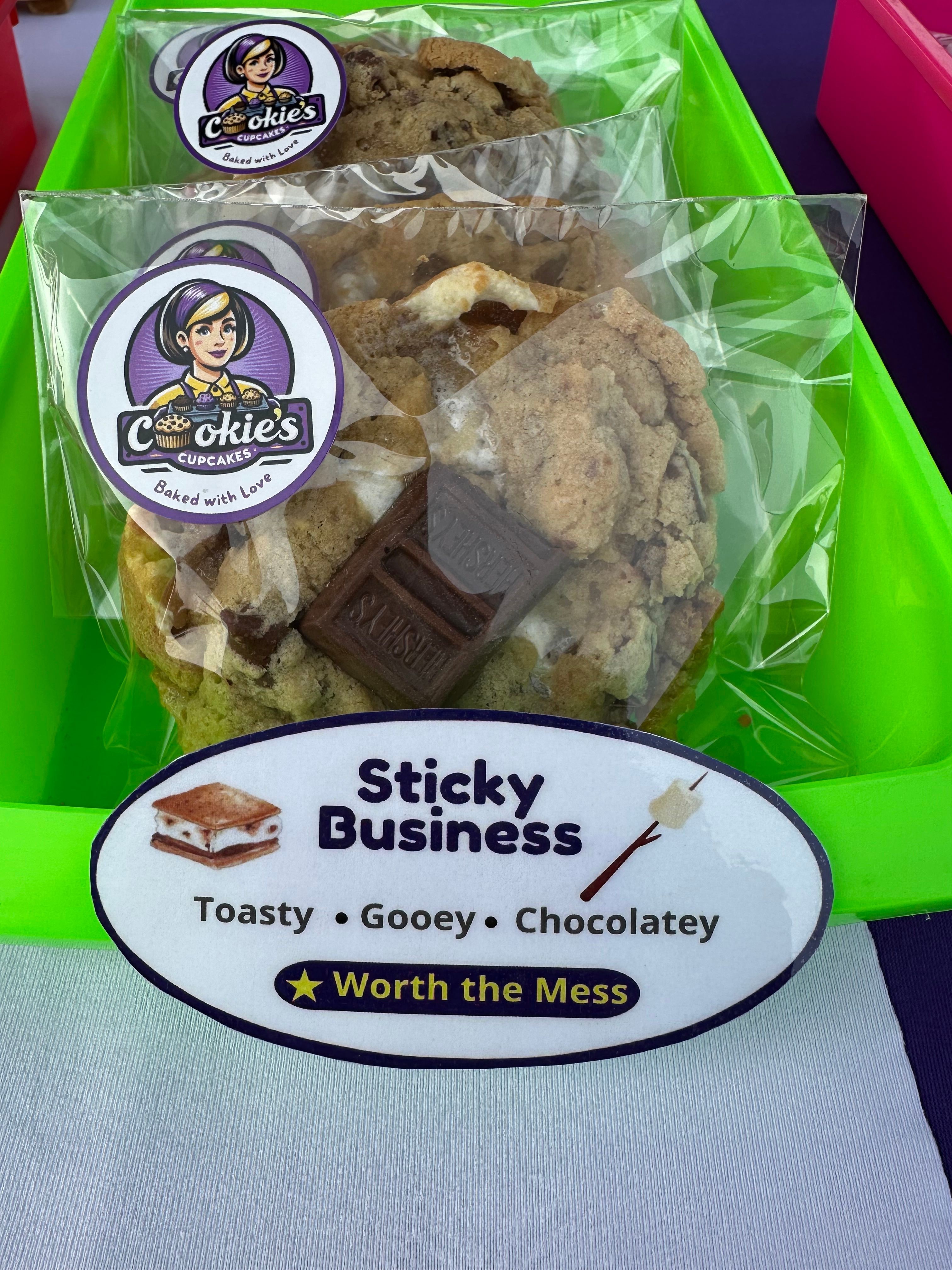 Clear plastic bag with cookies, a piece of chocolate, and a sticker label, placed on a green surface.