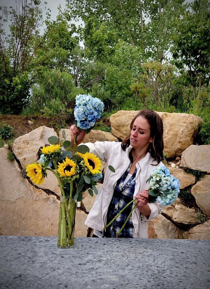 Woman holding blue hydrangeas outdoors with rocks and trees in background.