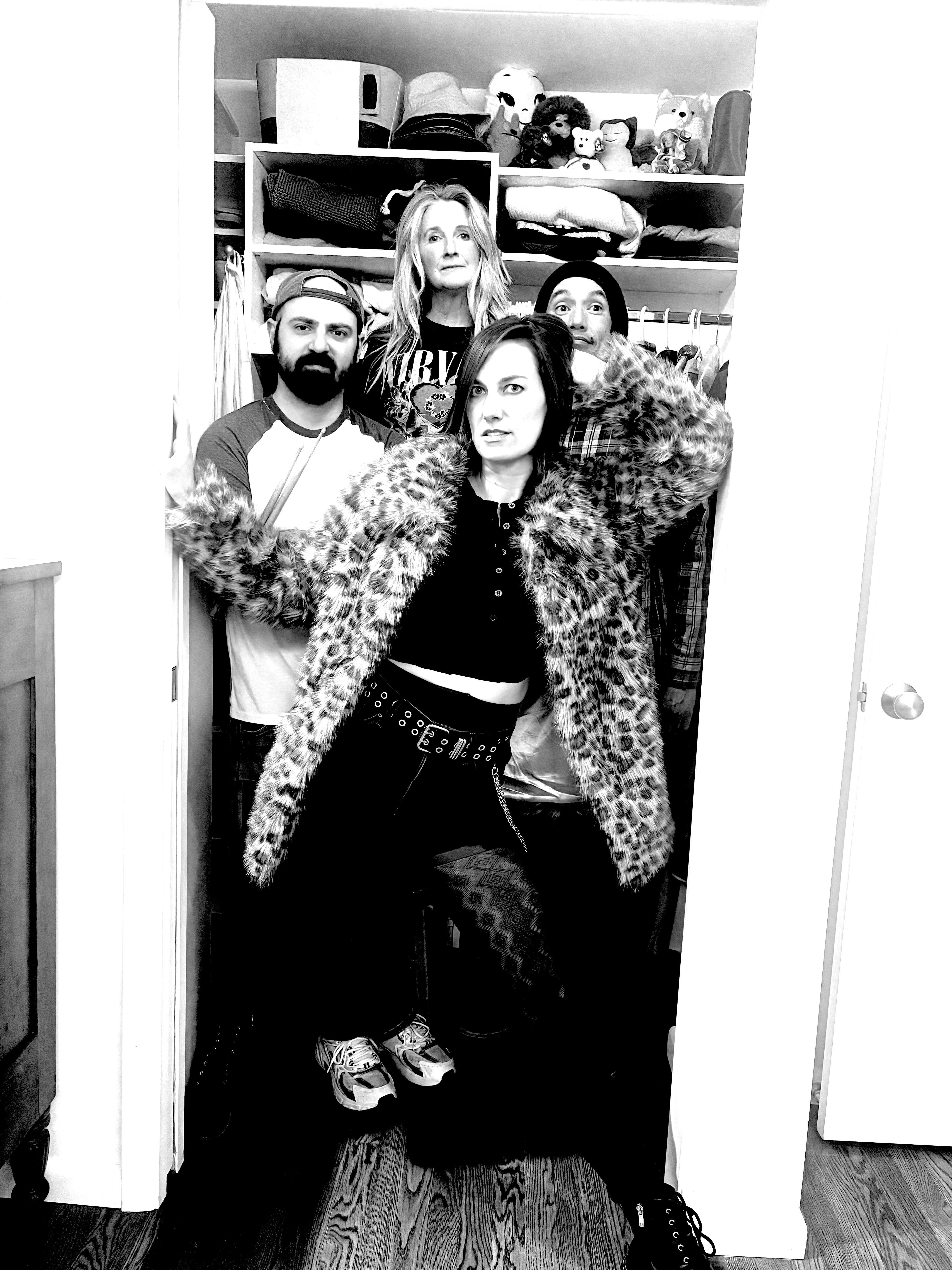 Group of five people taking a mirror selfie in a room with shelves and storage items behind them.