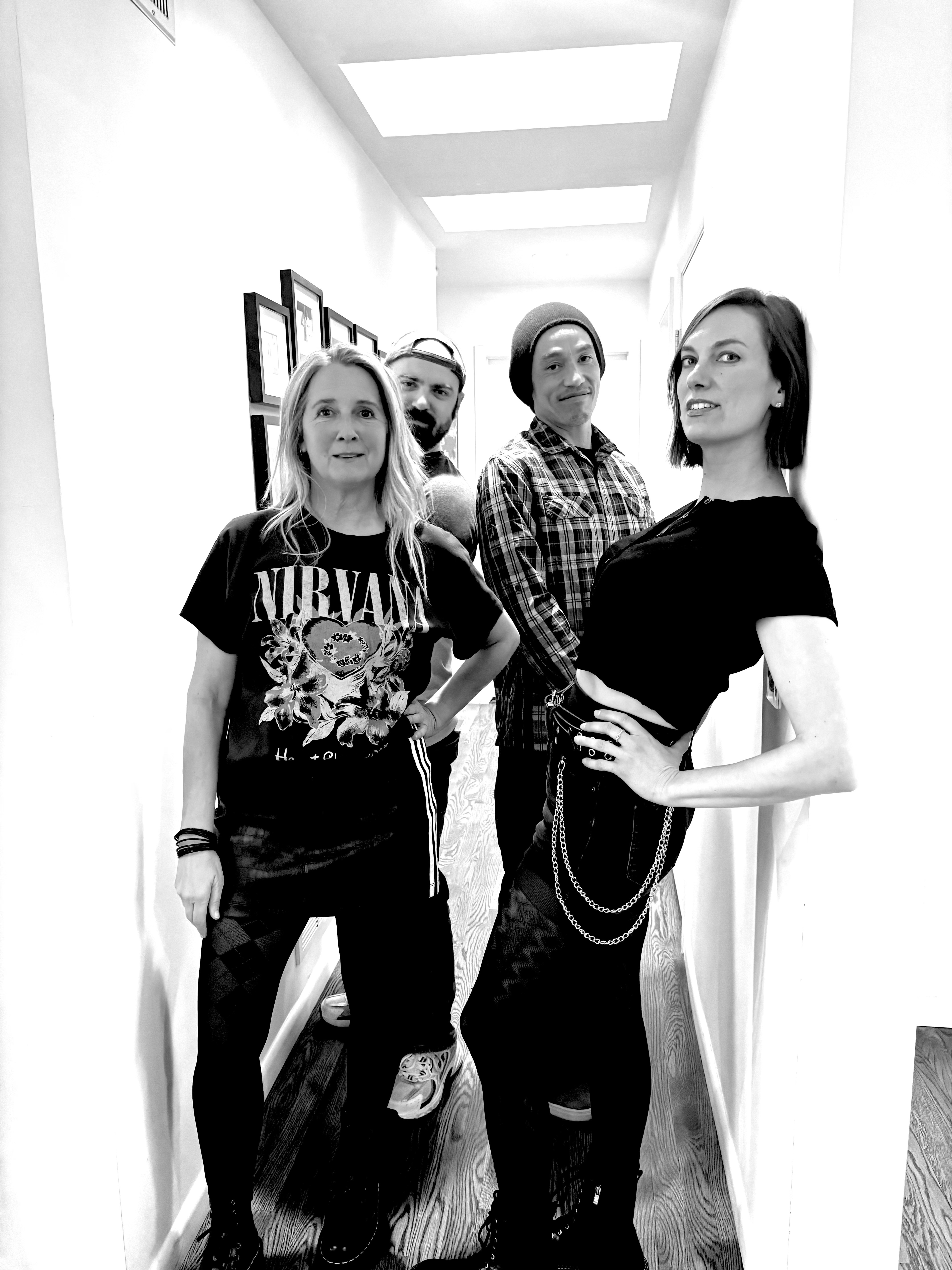 Four people standing in a hallway with framed pictures on the wall, posing for a photo, smiling and looking at the camera.