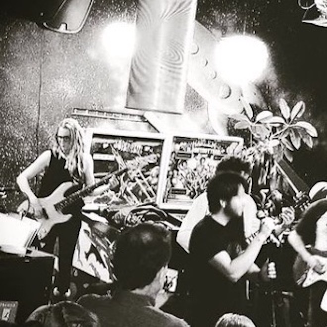 Band performing on stage with guitars, audience watching, and stage decorations visible, in black and white.