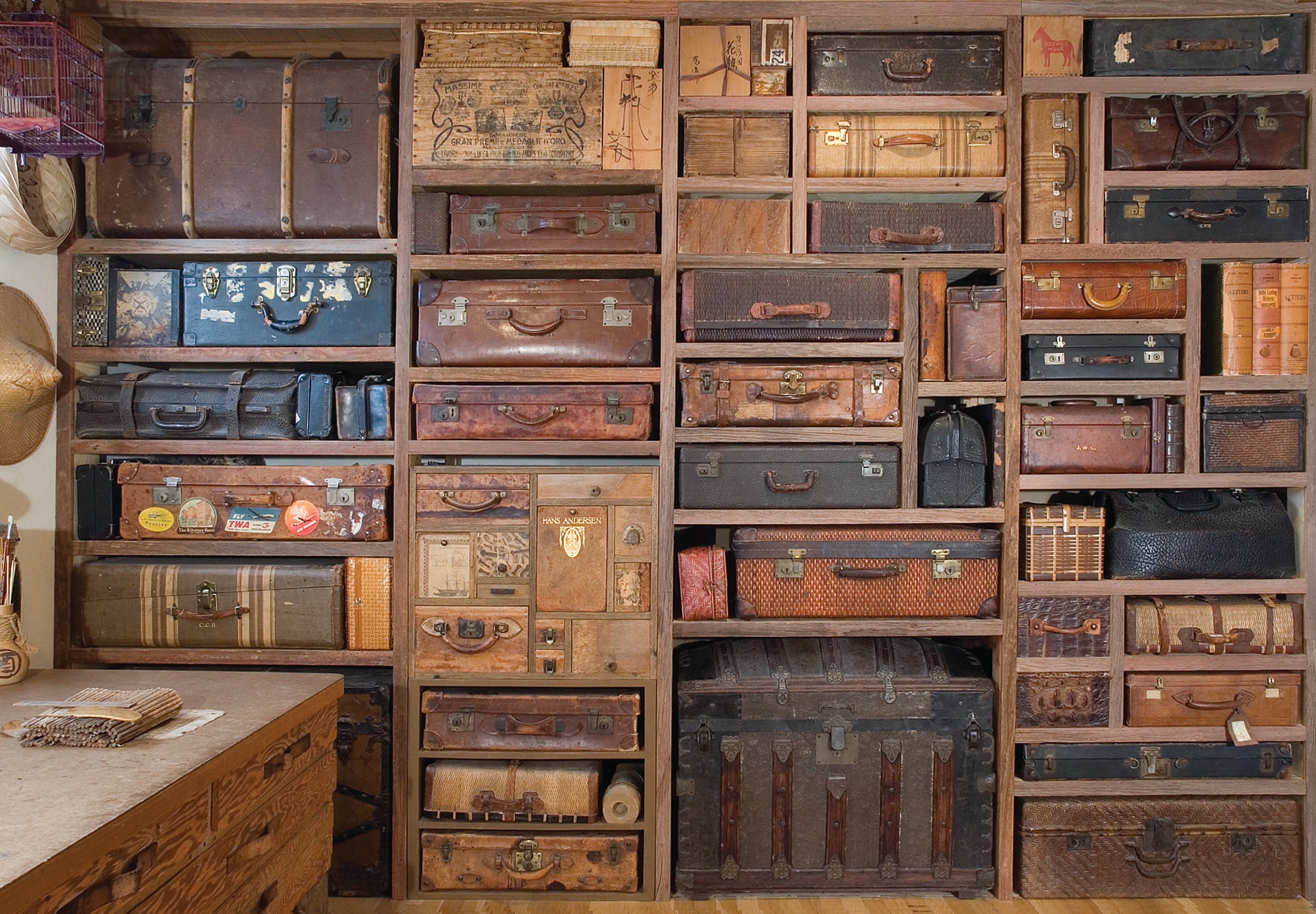 Wall filled with vintage suitcases and trunks of various sizes and colors, arranged in a grid pattern.