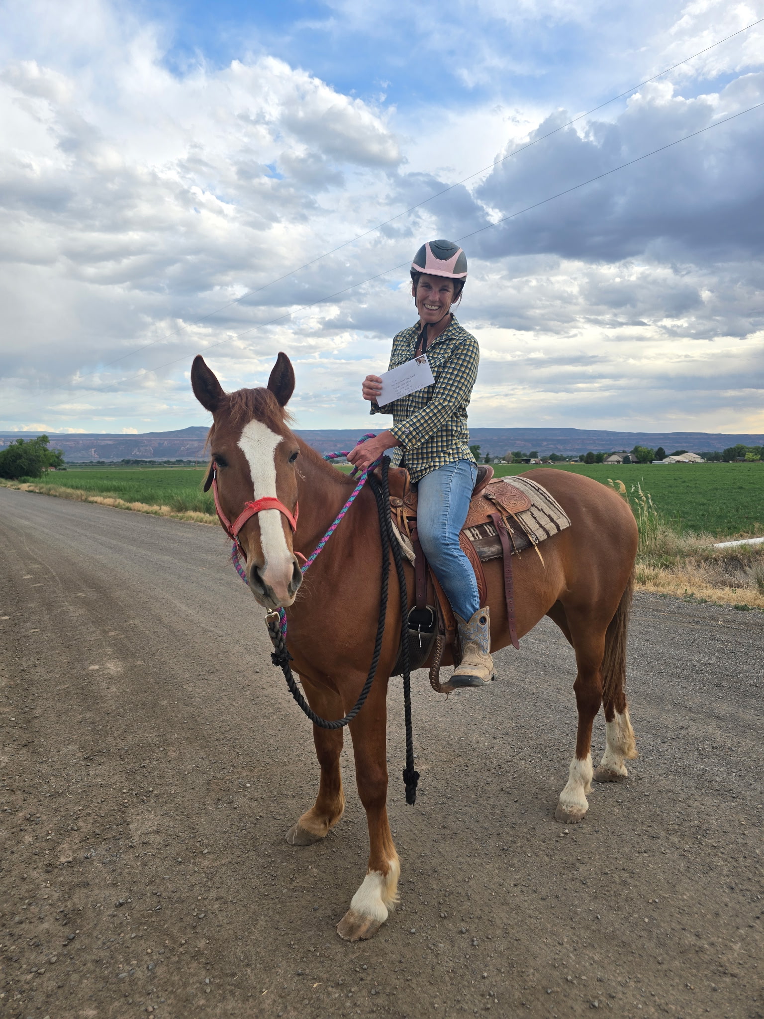 Child riding a brown and white horse on a dirt road with a cloudy sky and fields in the background.