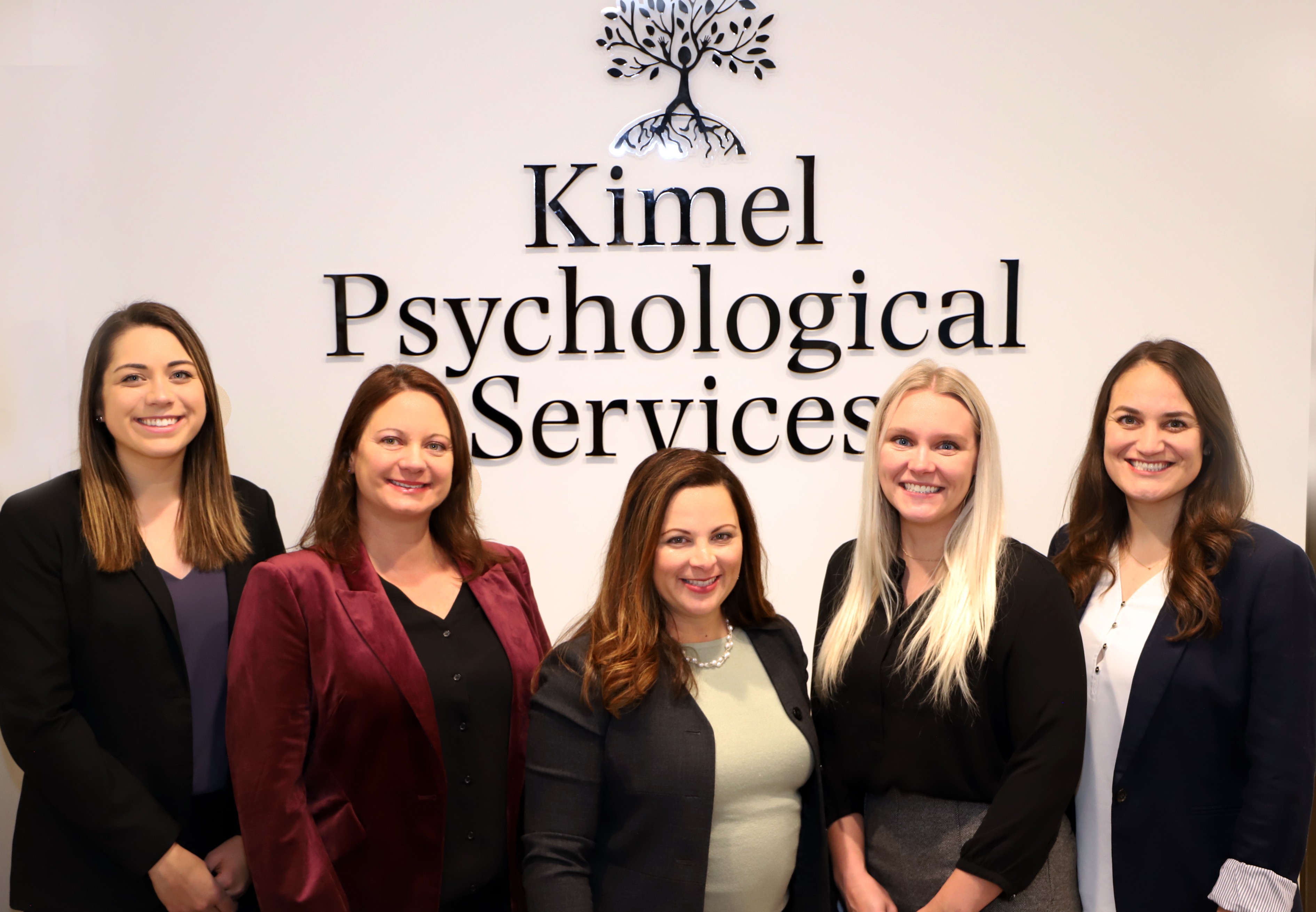 Five women standing in front of a wall with the text 'Kimel Psychological Services' and a tree logo.