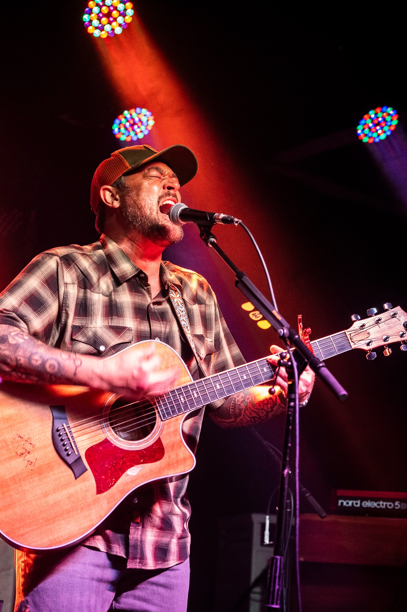 Man playing guitar and singing into microphone on stage with colorful lights overhead