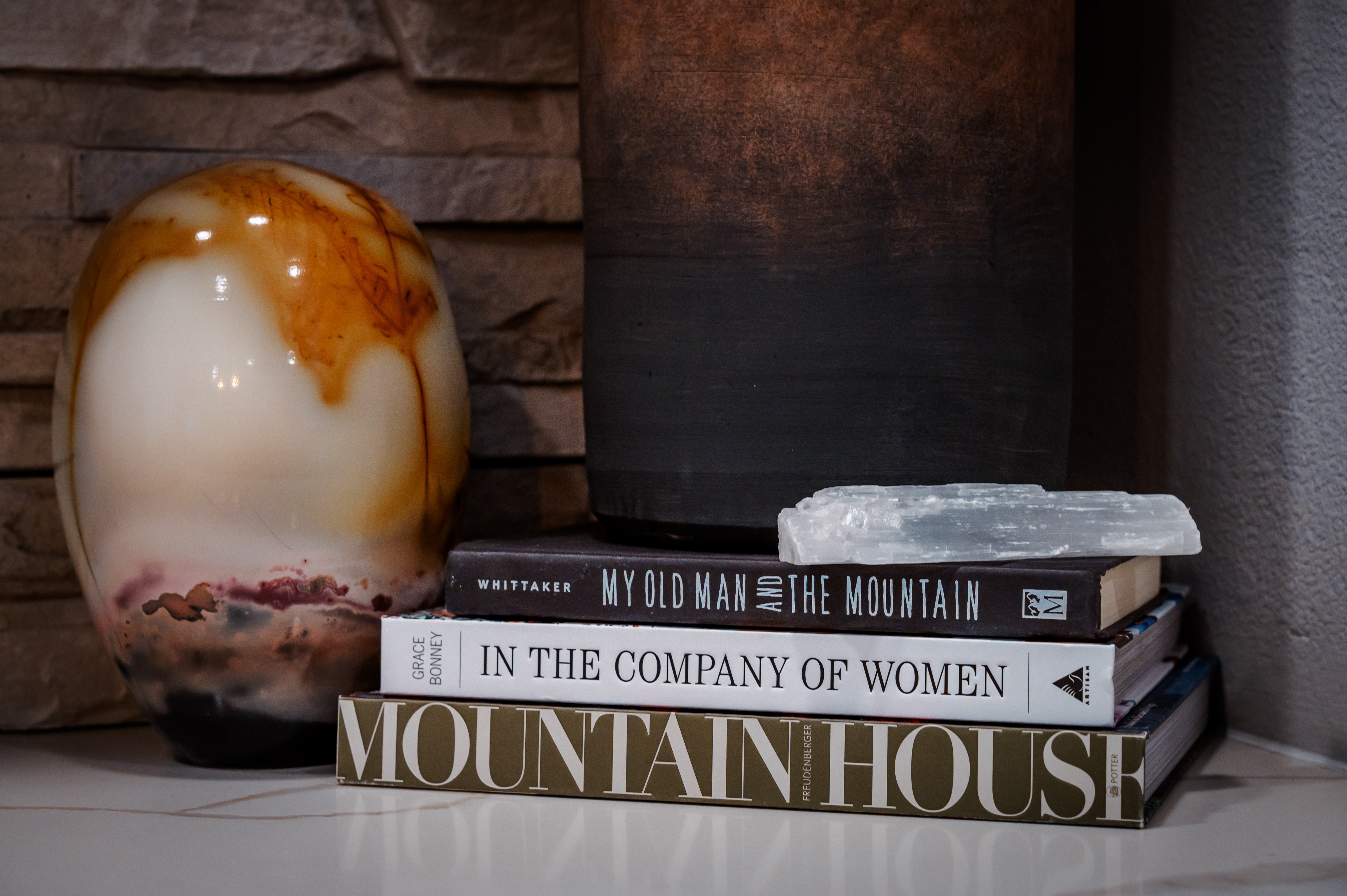 Stack of books and a decorative vase on a shelf against a brick wall.