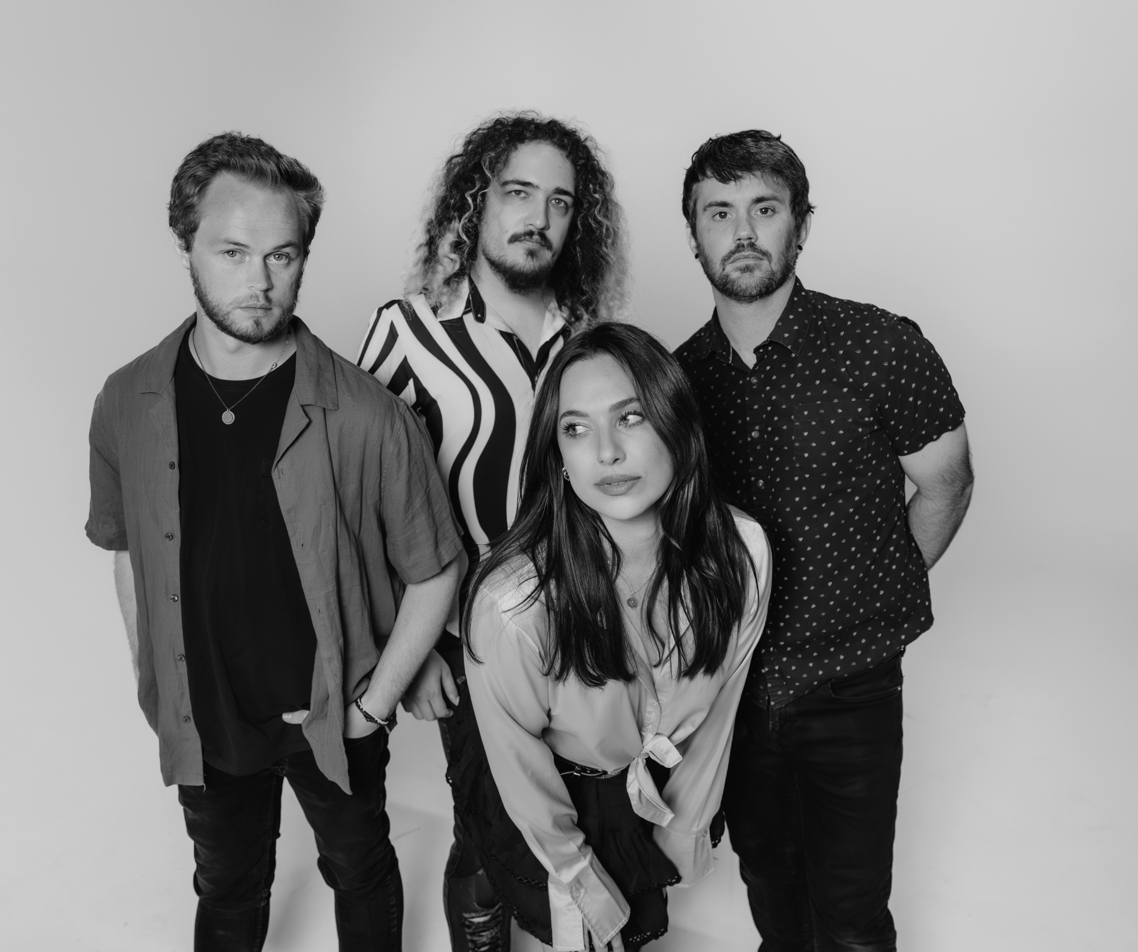 Four people standing together, two men and two women, in front of a plain background.