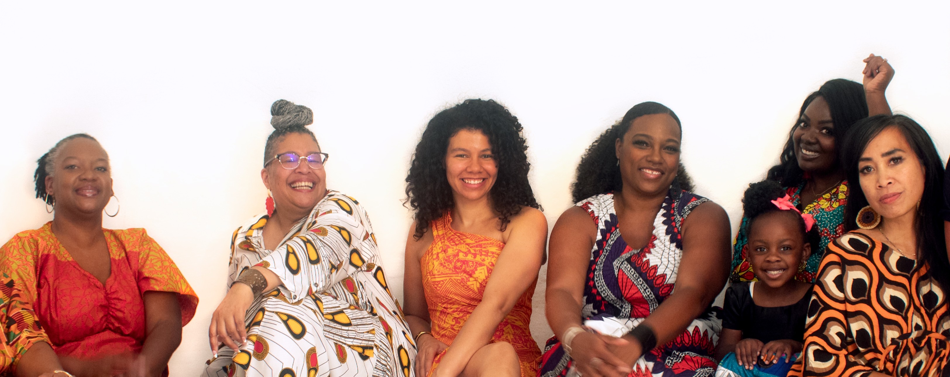 Six women and girls smiling, standing together against a white background, wearing colorful clothing.