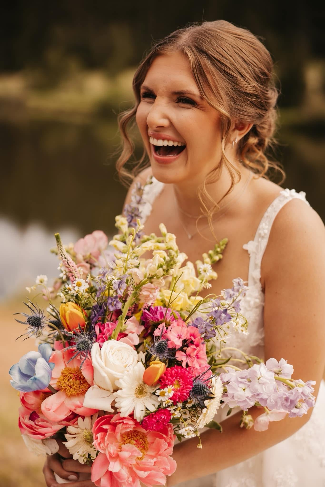 Young woman in wedding dress holding a colorful bouquet, smiling outdoors with blurred background.