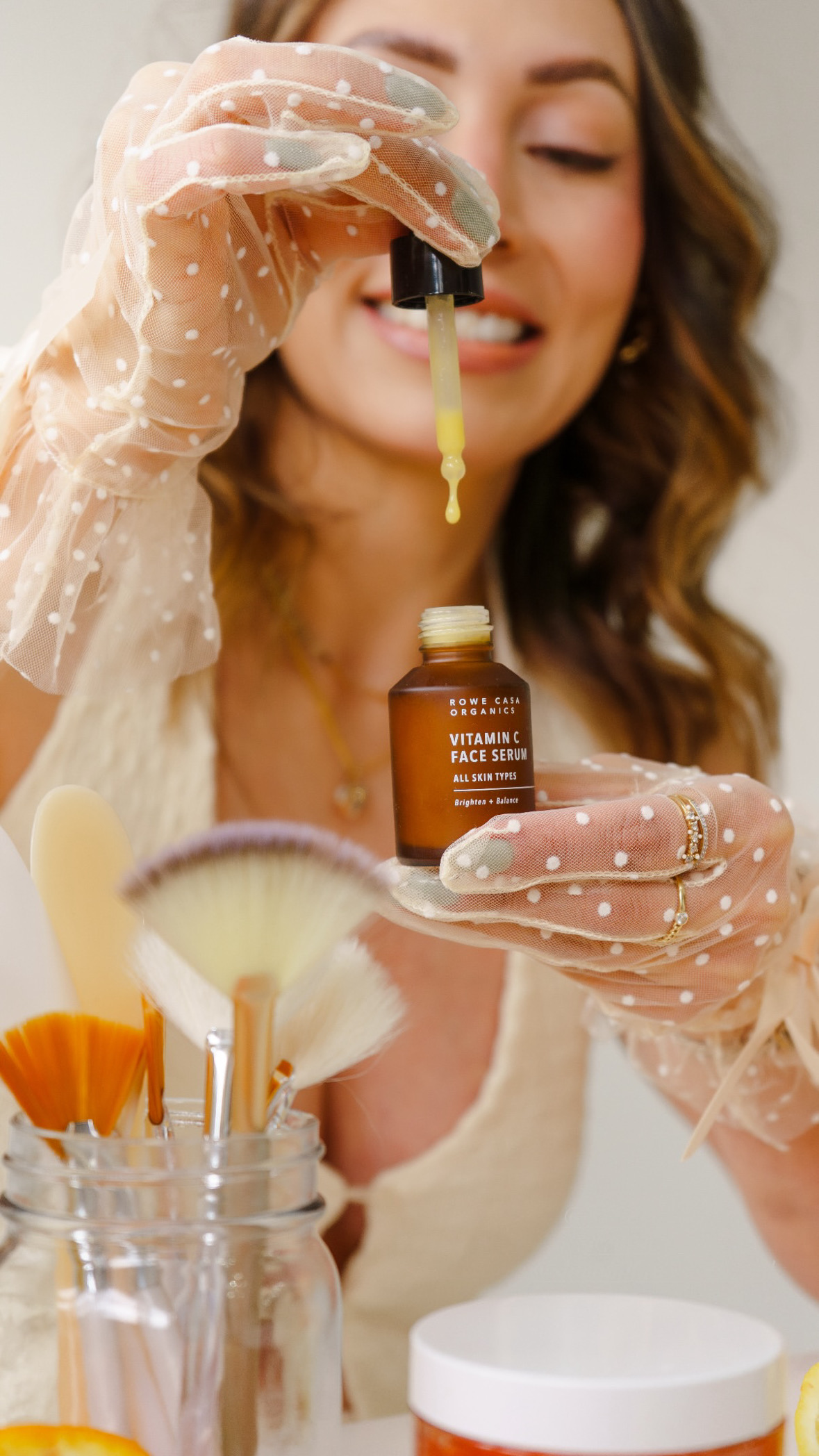 Woman holding a dropper bottle, dispensing liquid into her mouth, with skincare products nearby.