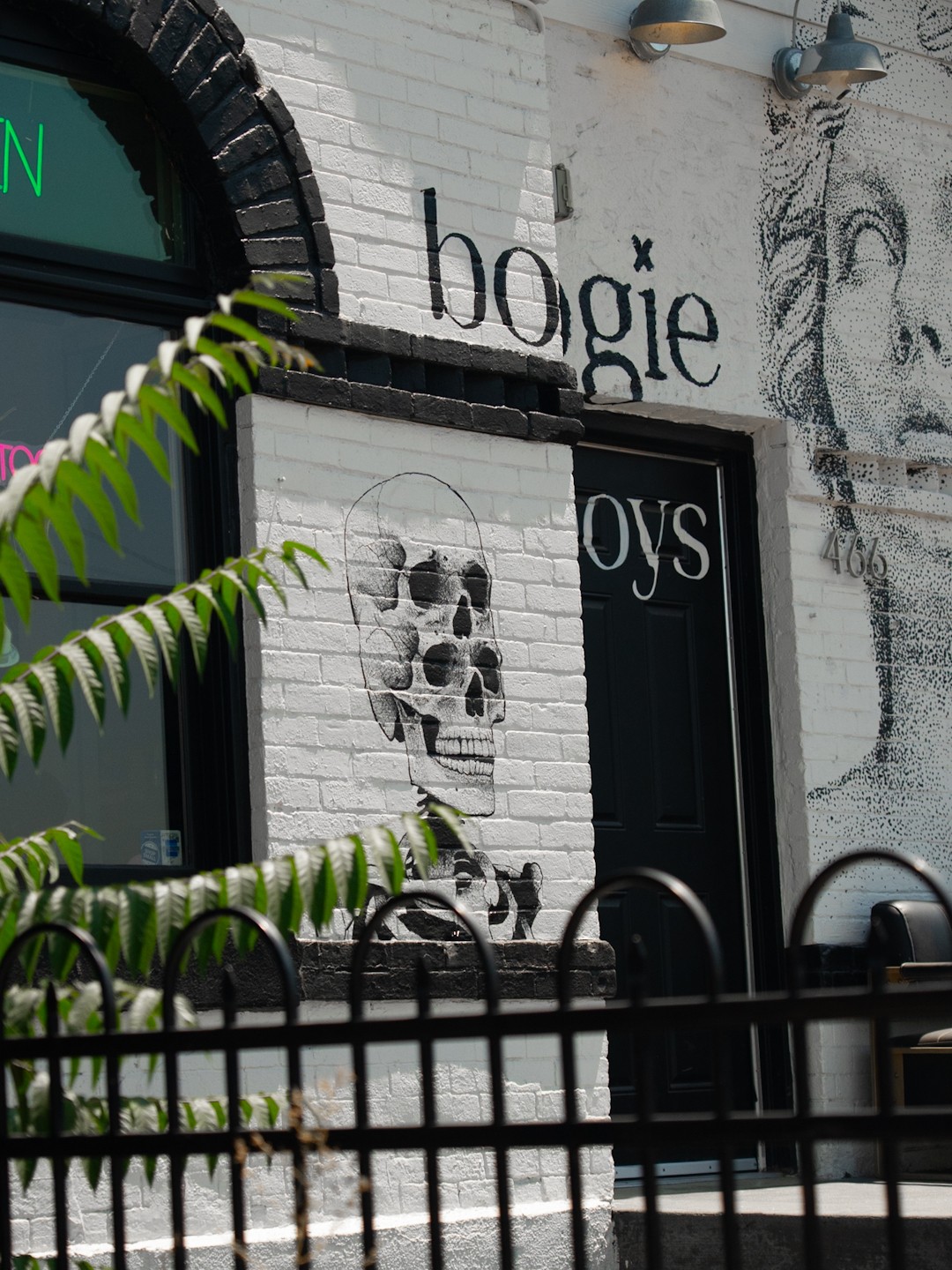 Brick wall with graffiti art of a skull and the words 'bogie boys' on a building exterior, with a plant in foreground.