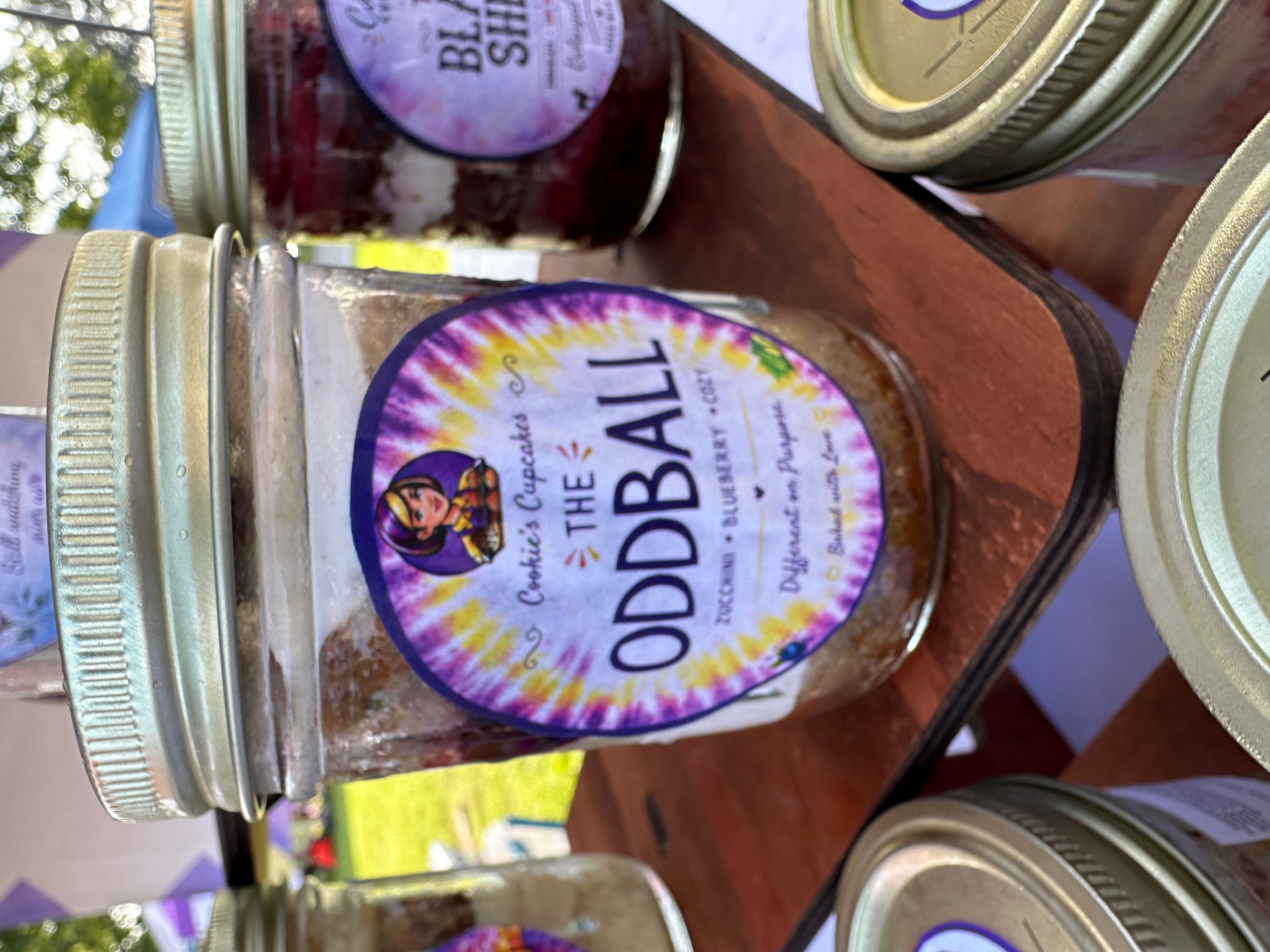 Jar with a label reading 'The Oddball' and a colorful design, placed on a wooden surface with other jars around.