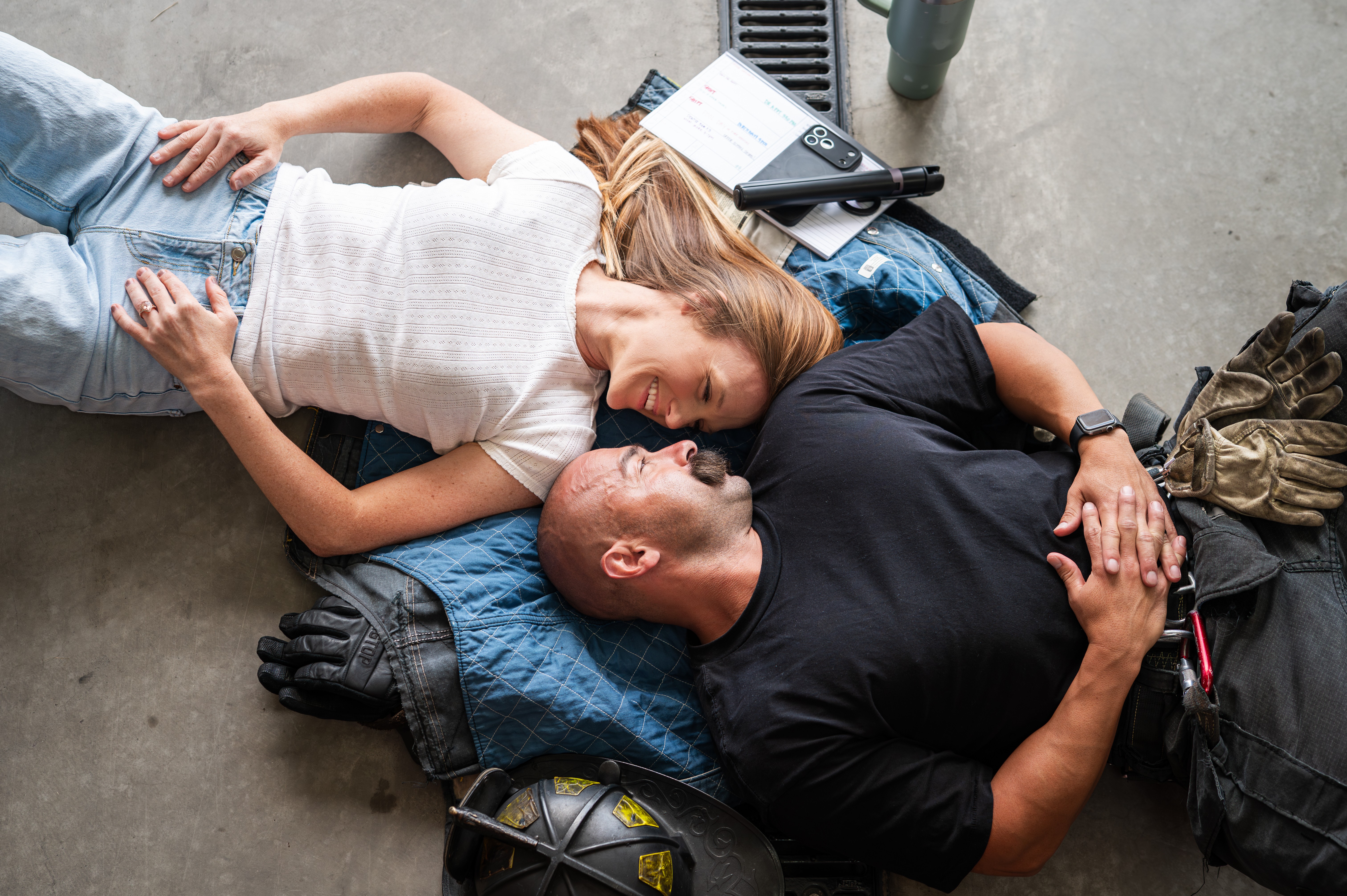 Two people lying on the ground, facing each other, with various items around them, including gloves and a backpack.