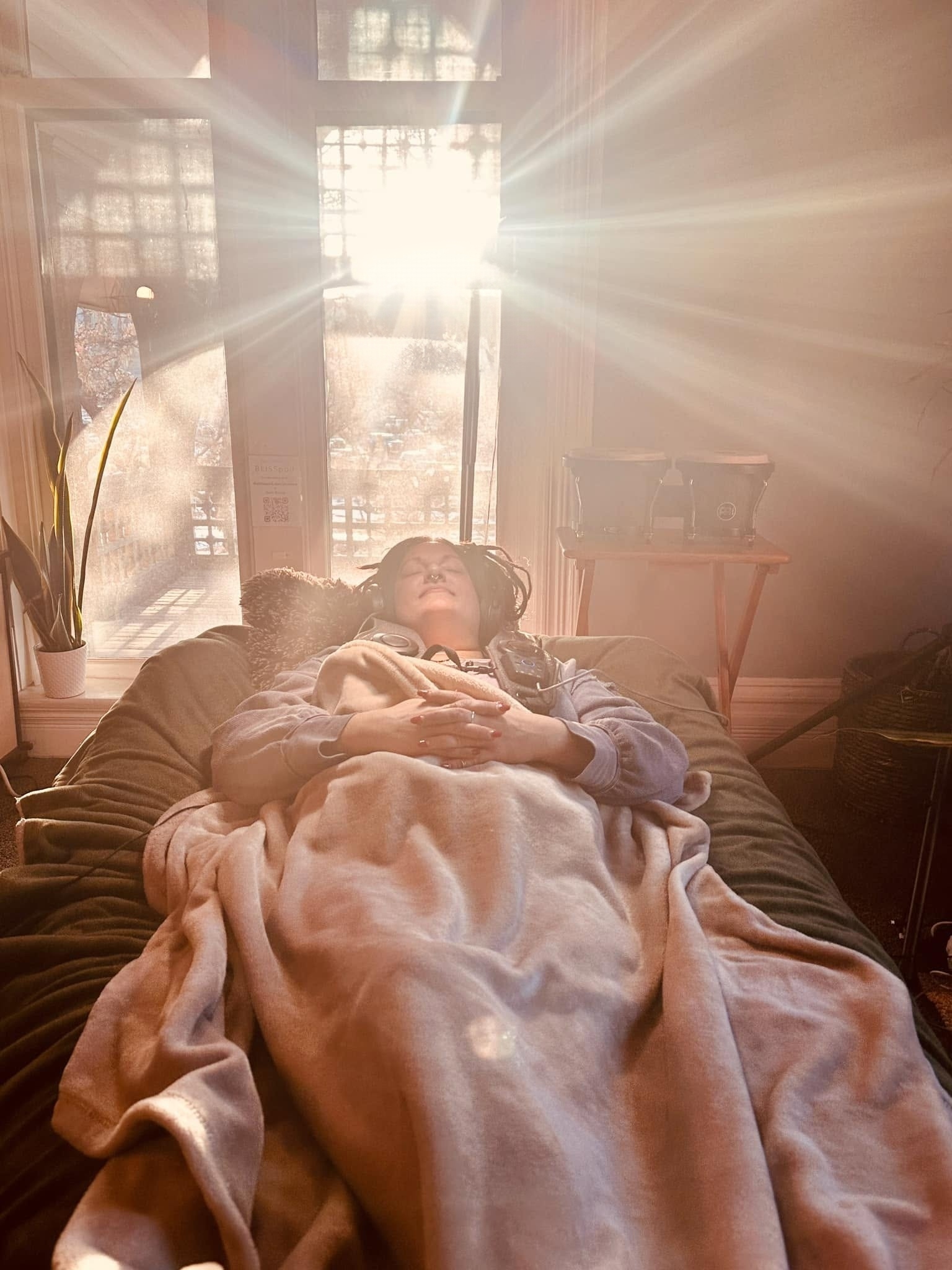 Person lying on a couch with sunlight streaming through a window behind them, covered with a blanket.