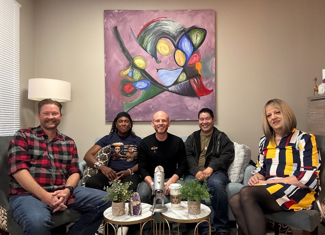 Five people sitting on a couch in a room with a colorful abstract painting on the wall behind them.