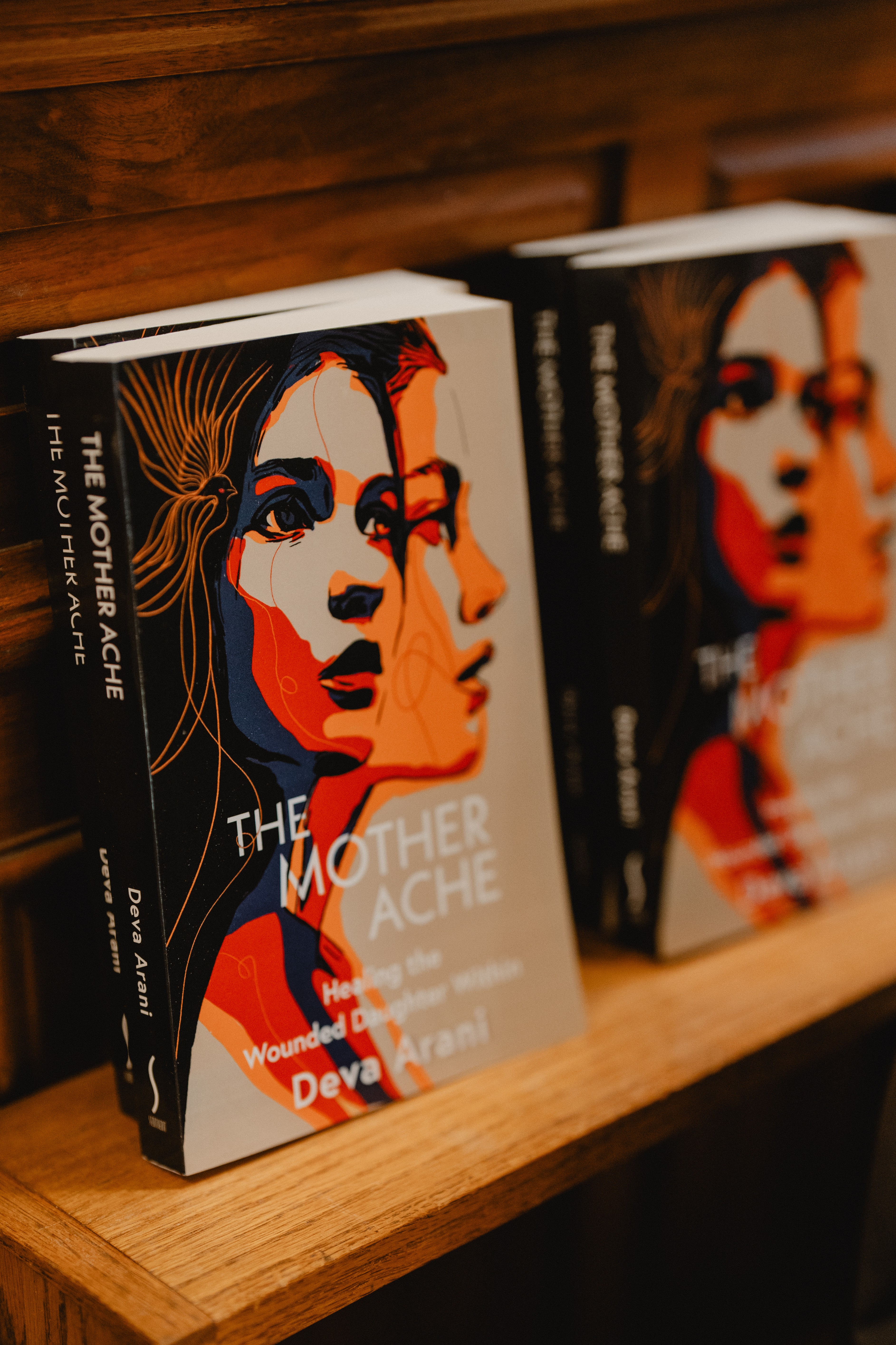 Two books on a wooden shelf, one titled 'The Mother Wound' with a colorful illustrated woman's face on the cover.