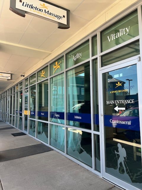 Glass entrance doors with signs and reflections, Littecom Massage sign on wall, and a sidewalk outside.