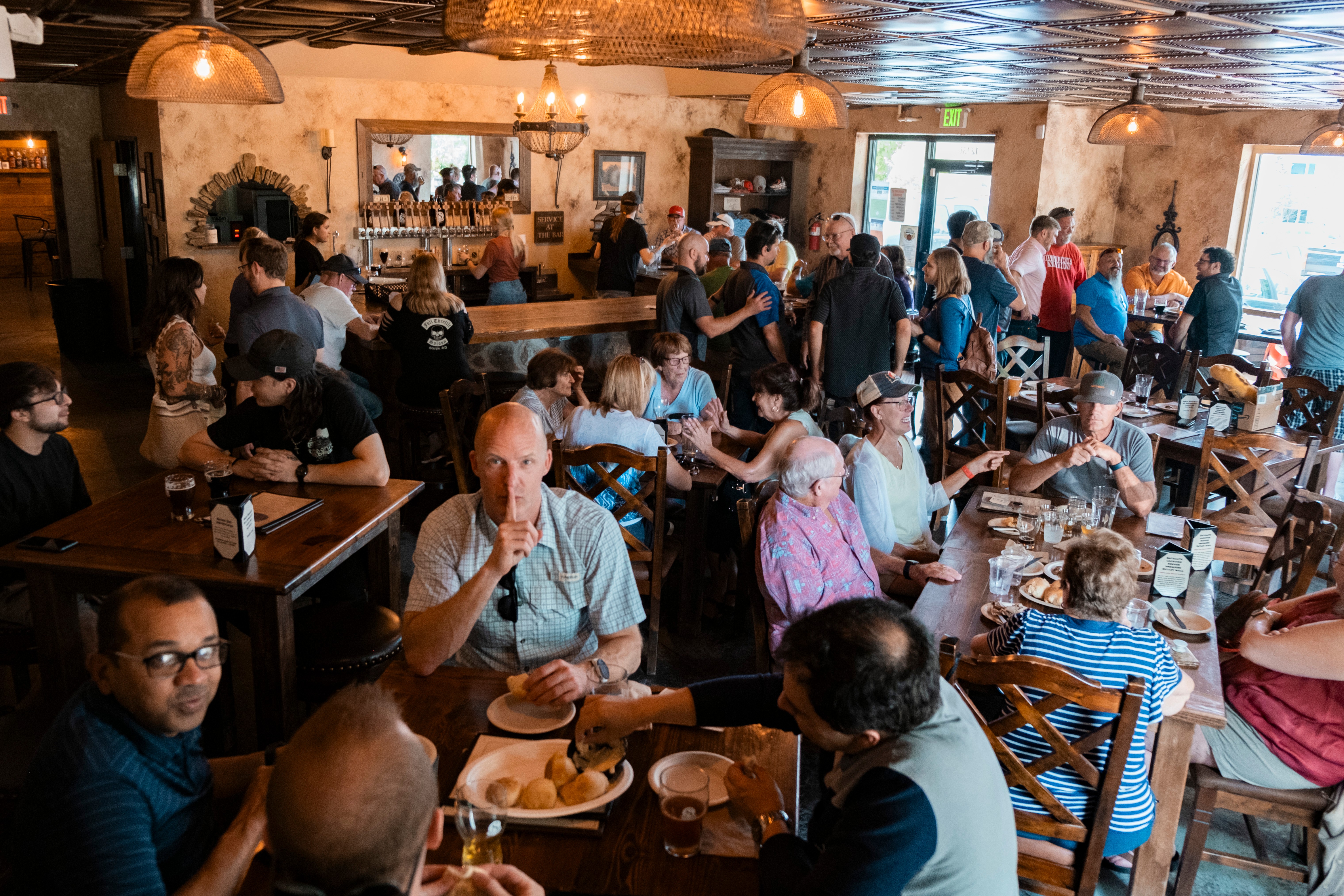 People dining and socializing in a busy restaurant with wooden furniture and warm lighting.