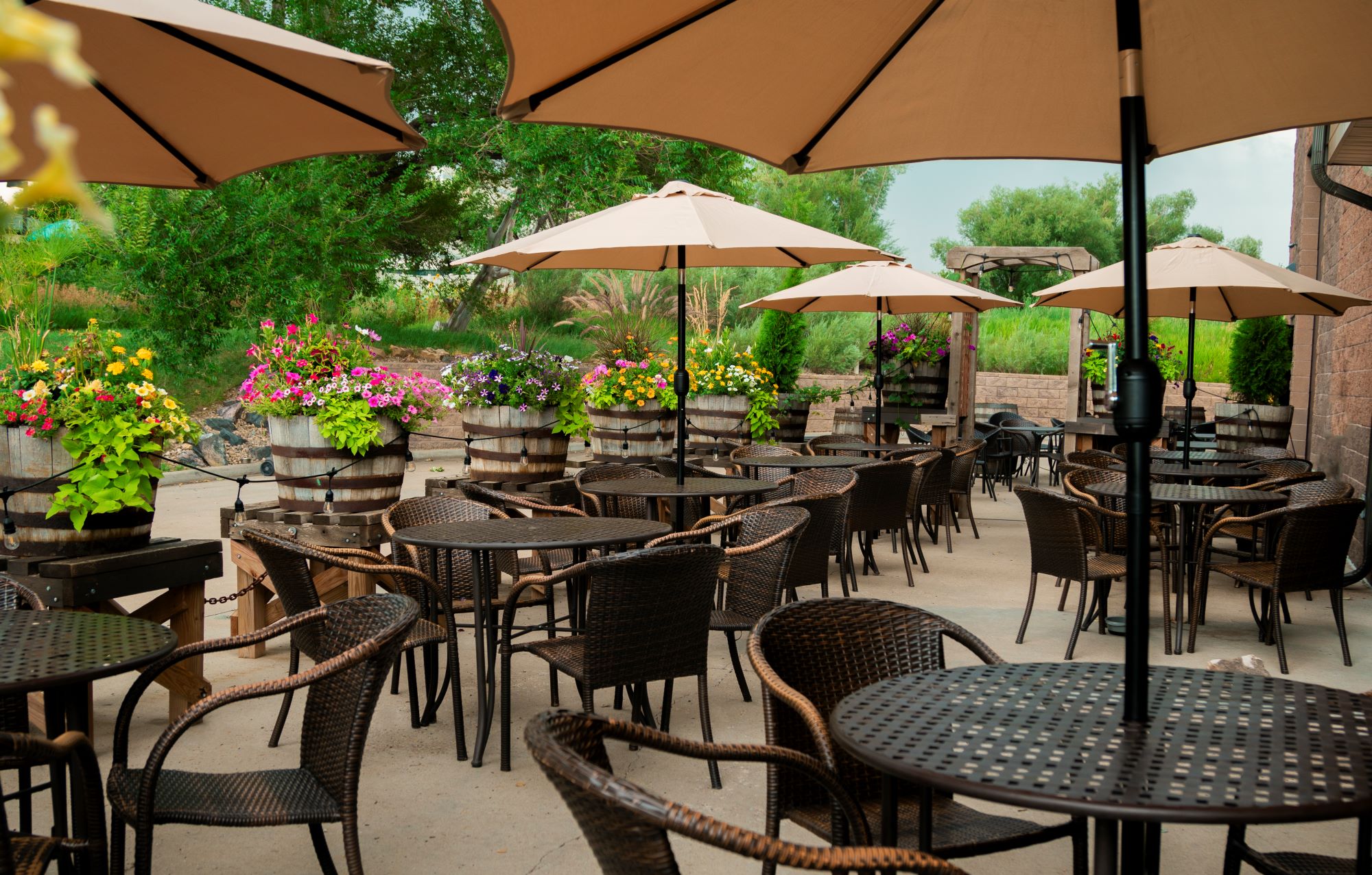Outdoor patio with tables, chairs, and umbrellas, surrounded by greenery and flowers.