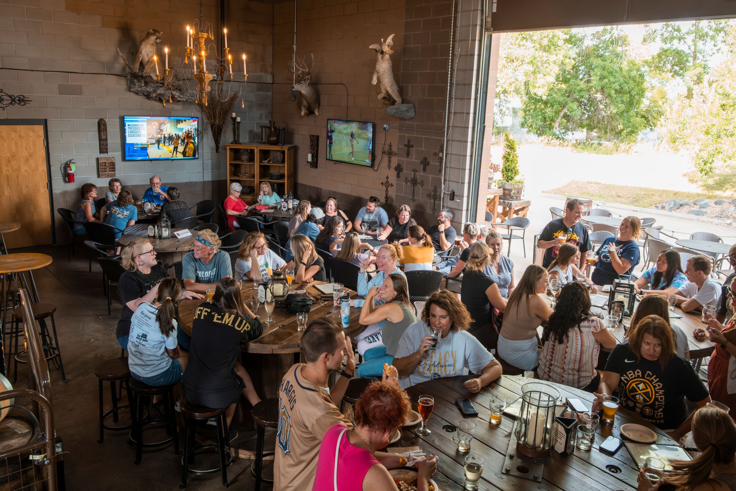 Crowded restaurant with people dining at tables, large windows, and outdoor view, warm lighting, and decorative wall art.