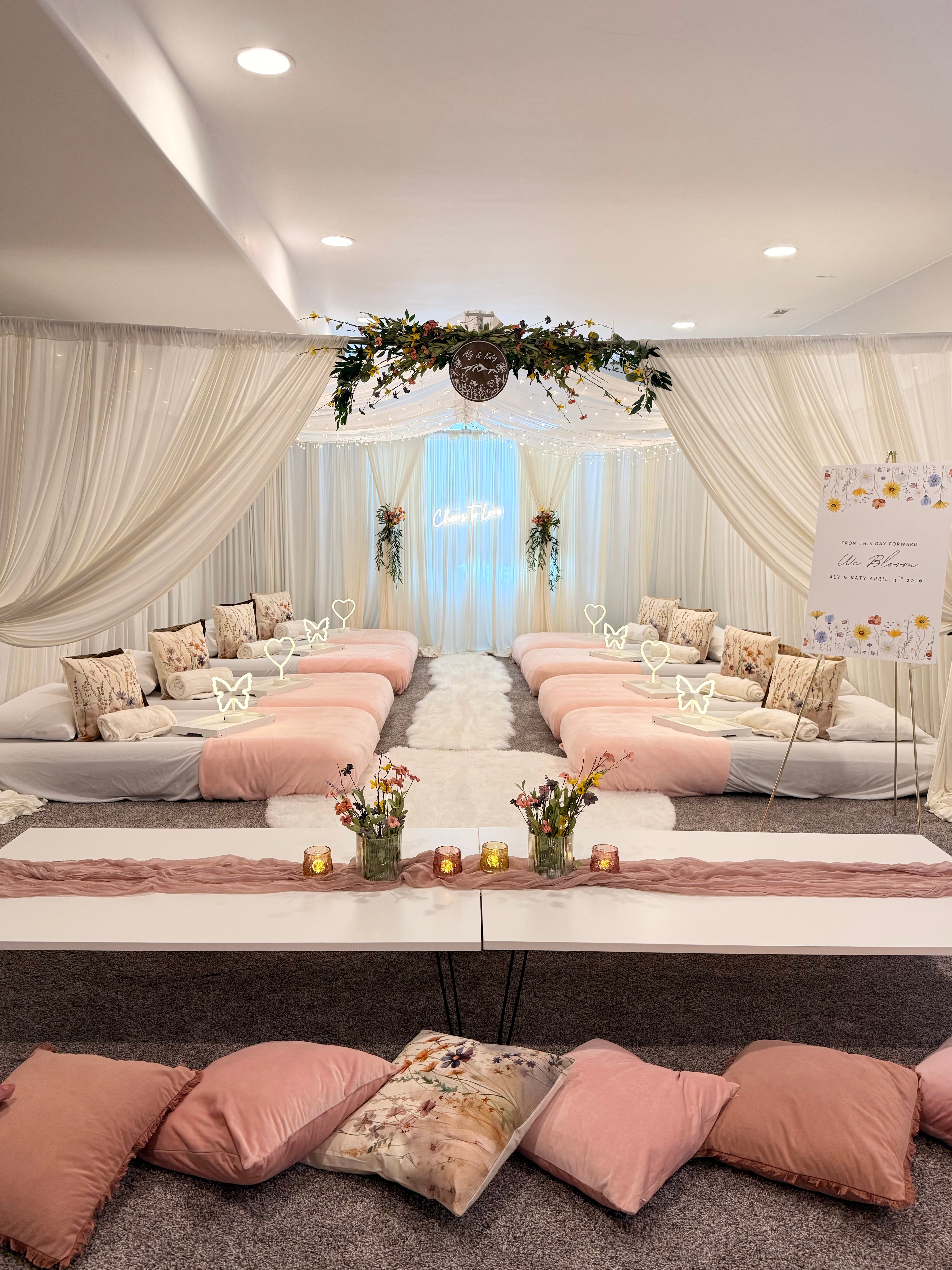 Elegant indoor event space with draped curtains, floral decorations, and seating arrangements with pink and beige cushions.