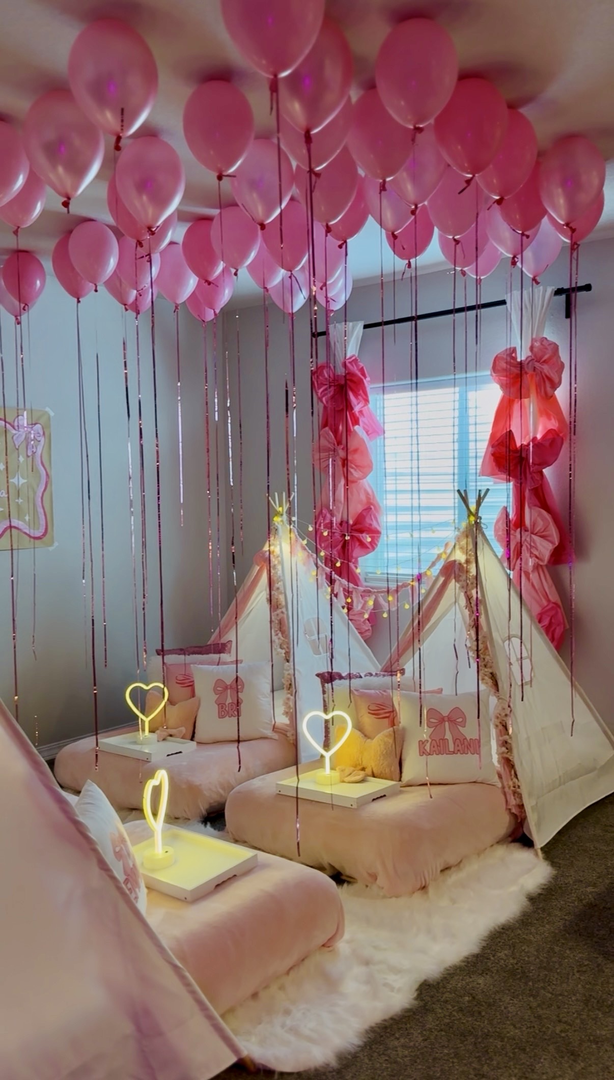 Decorated room with pink balloons hanging from ceiling, pink and red ribbons, a small tent, and seating area with cushions on a white rug.