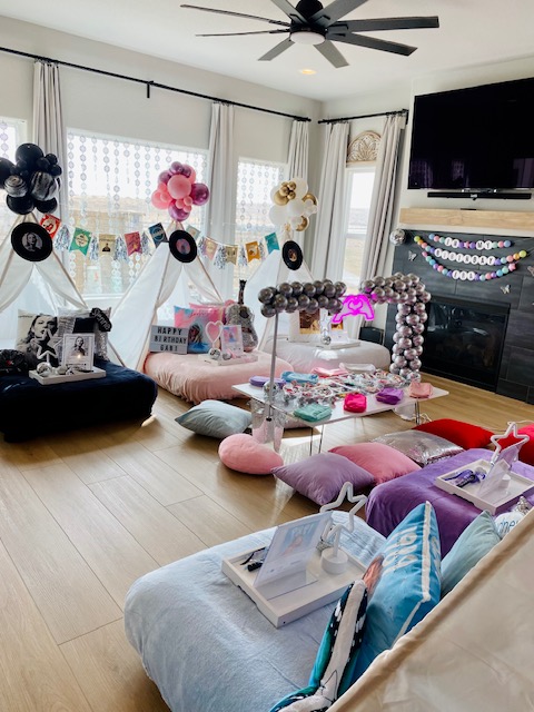Living room decorated with balloons, banners, and cushions, featuring a large TV, a fireplace, and a ceiling fan.
