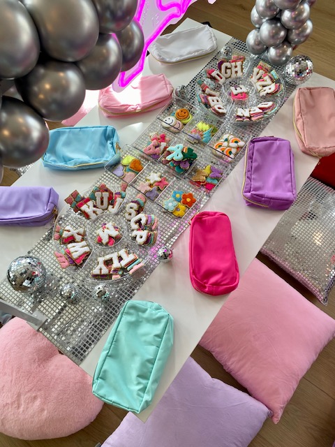 Table decorated with colorful wrapped gifts, party favors, and festive decorations, surrounded by pastel pillows and balloons.