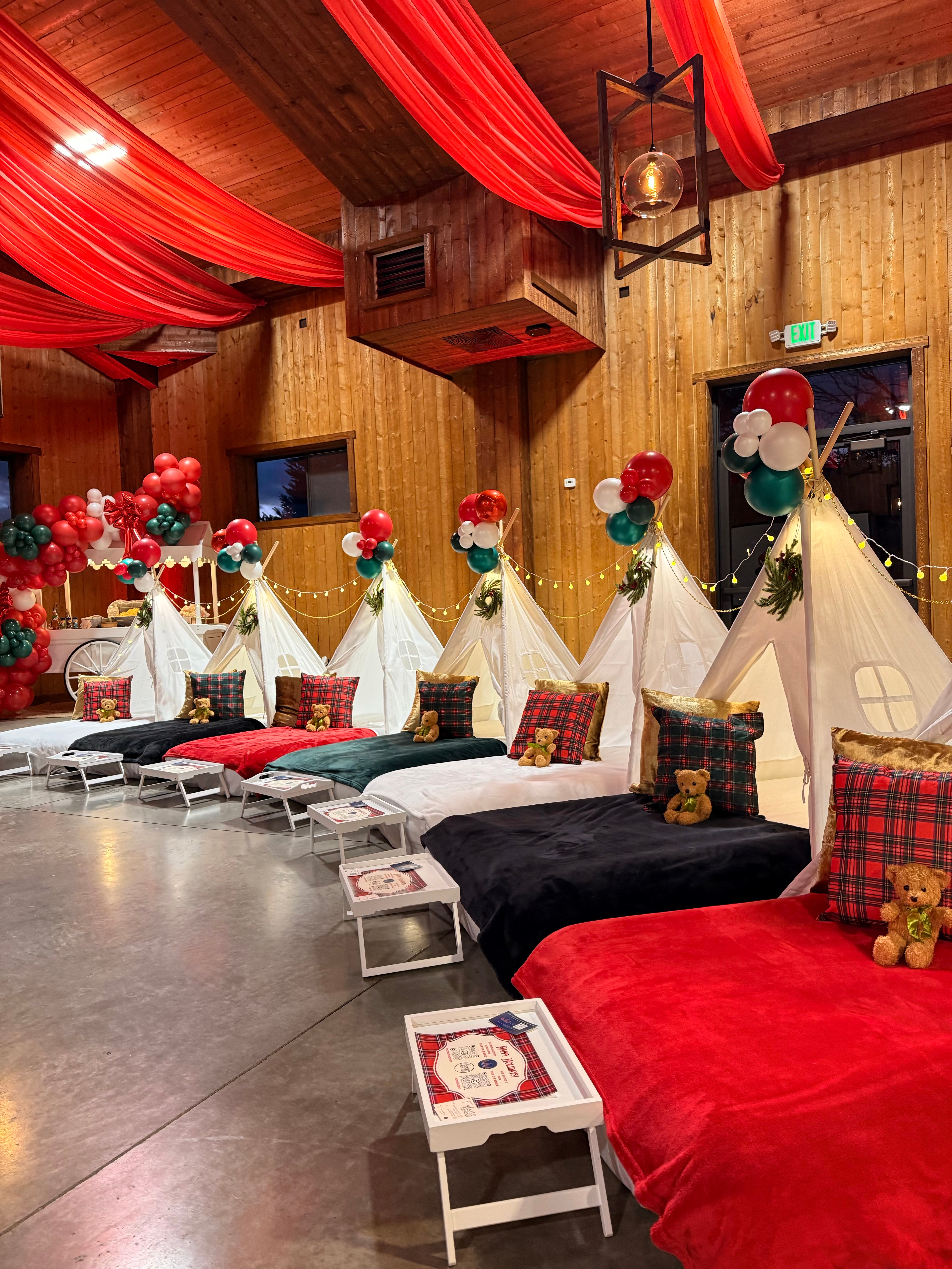 Room decorated with red drapes, balloon arrangements, and beds with colorful pillows and teddy bears, wooden walls and ceiling.