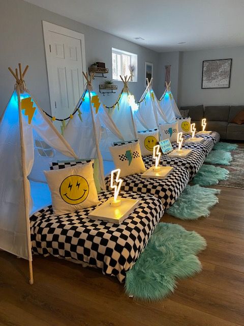 Party setup with checkered tablecloth, green fluffy rugs, and yellow pillows with smiley faces, decorated with blue and white streamers.