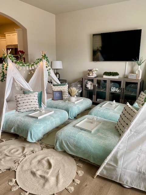Living room with light blue furniture, decorated with string lights, pillows, a TV, and a small table, in a cozy setting.