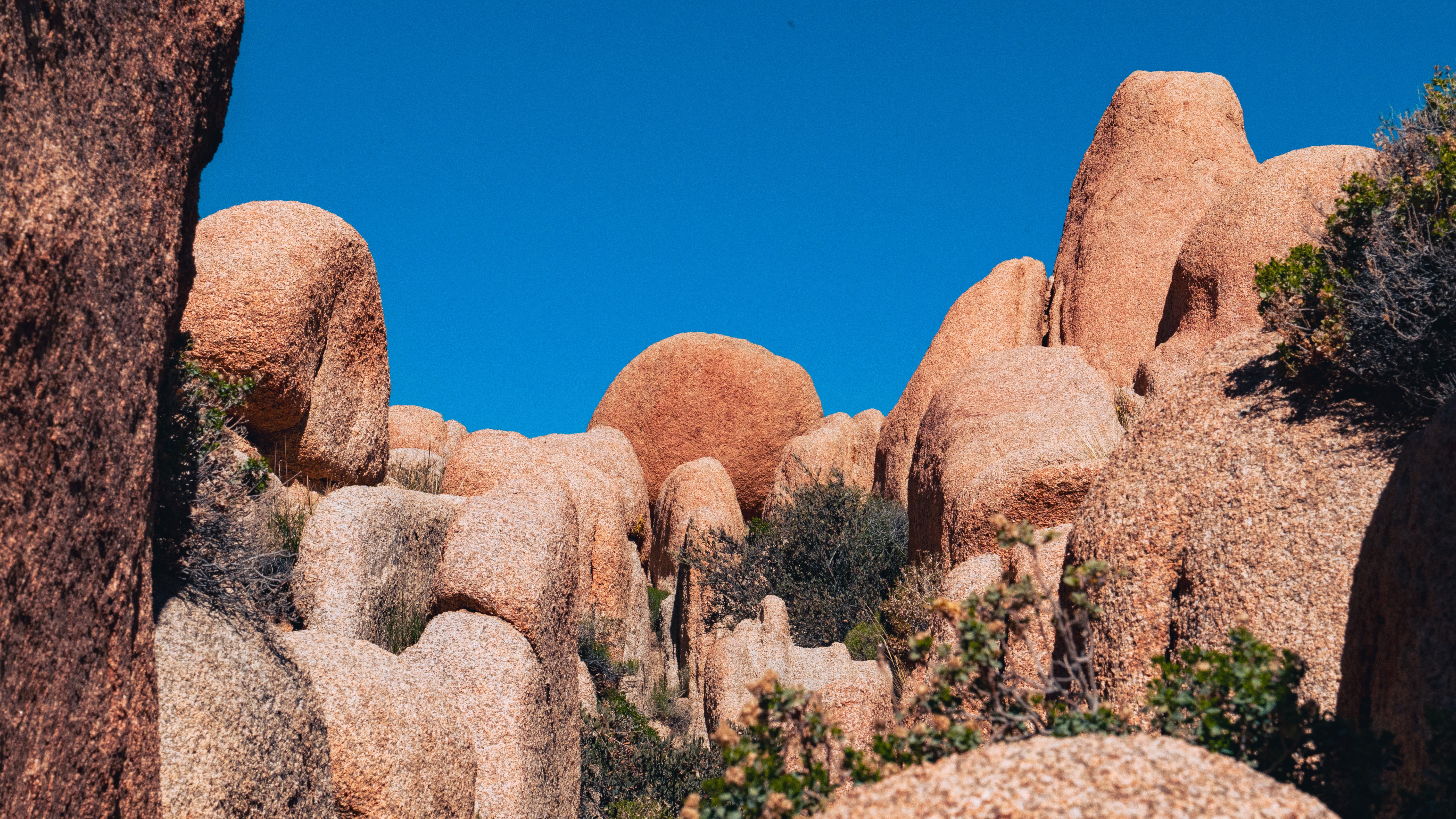 Rock formations with a clear blue sky in the background, some greenery at the base, and large rounded rocks.
