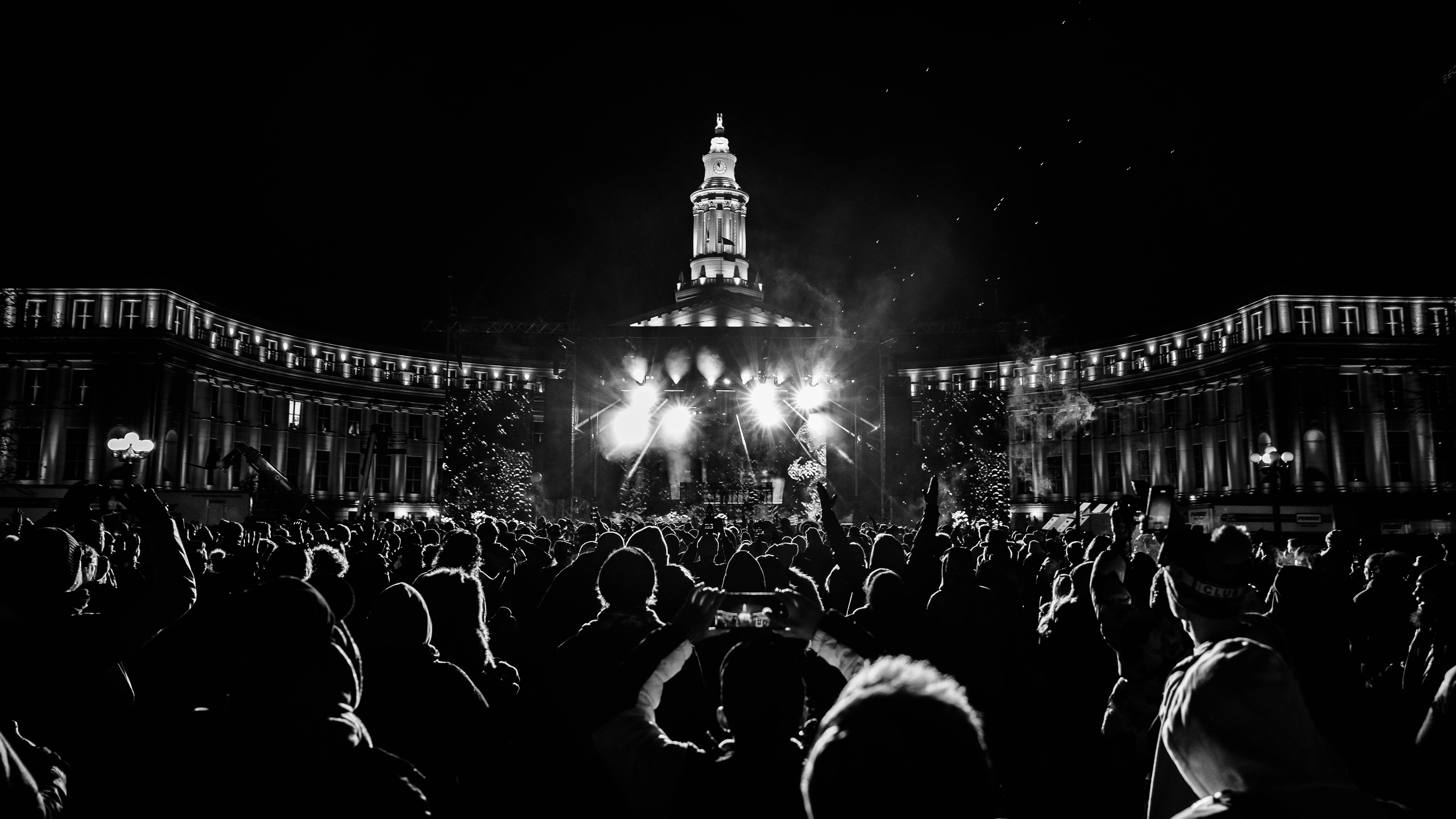 Crowd gathered in front of a lit building with a tall tower at night, illuminated by bright lights.