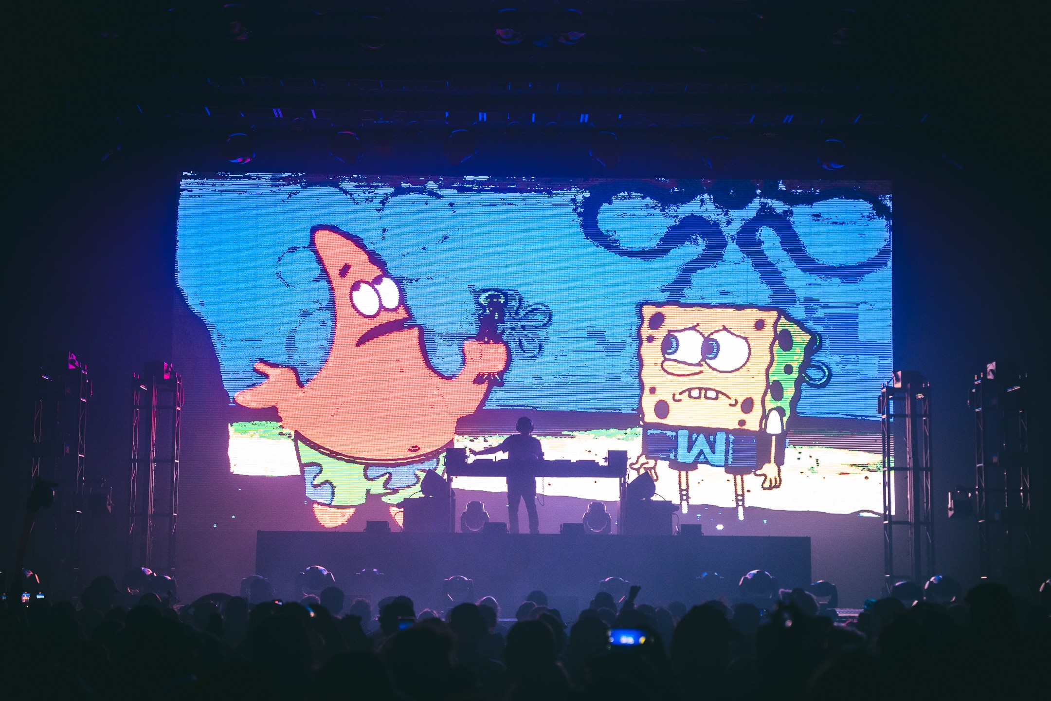 Large screen displays animated characters SpongeBob SquarePants and Patrick Star with a blue background, audience silhouettes at the bottom.
