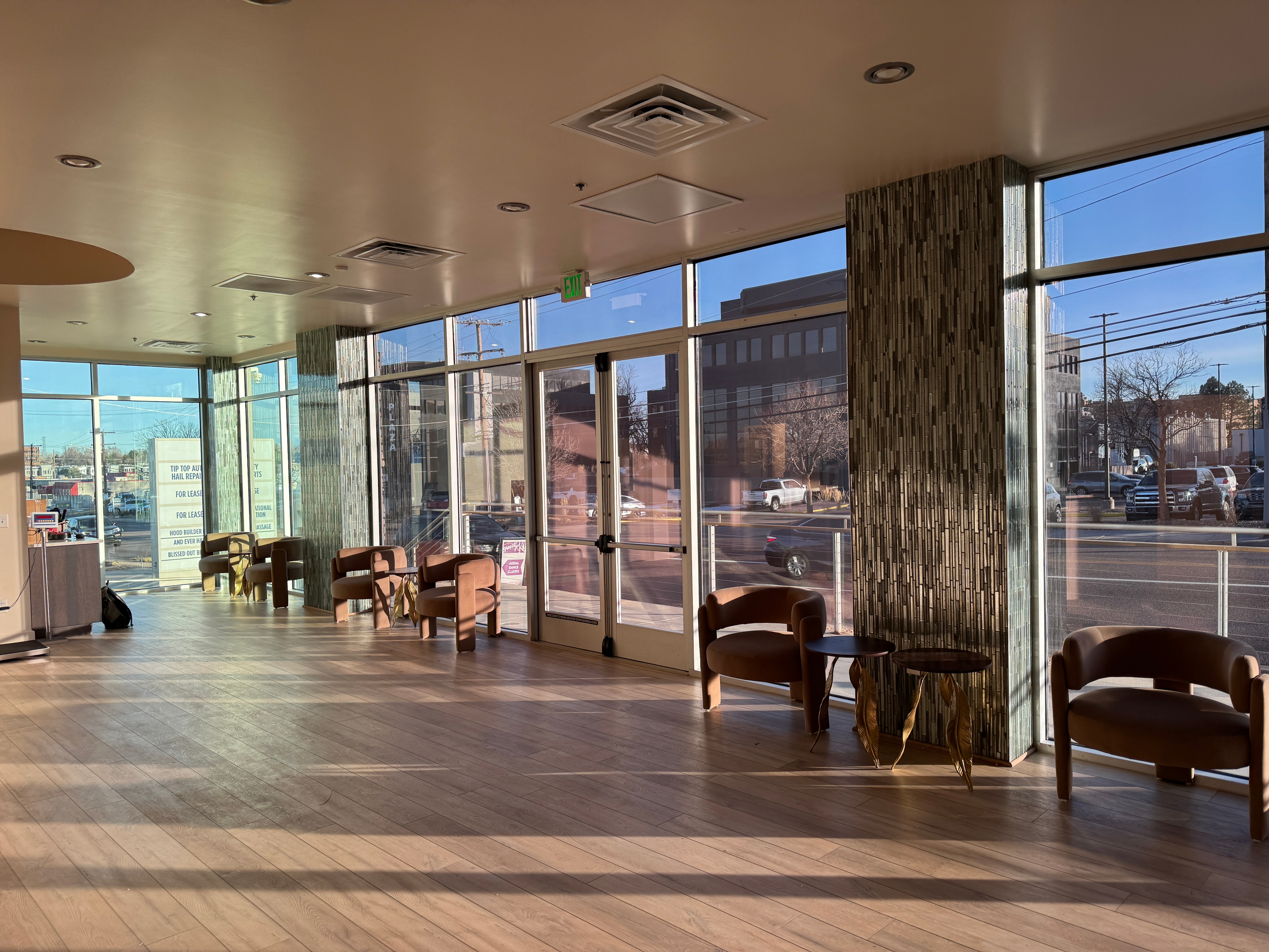 Spacious room with large windows, chairs, and a view of the street outside, sunlight casting shadows on the floor.