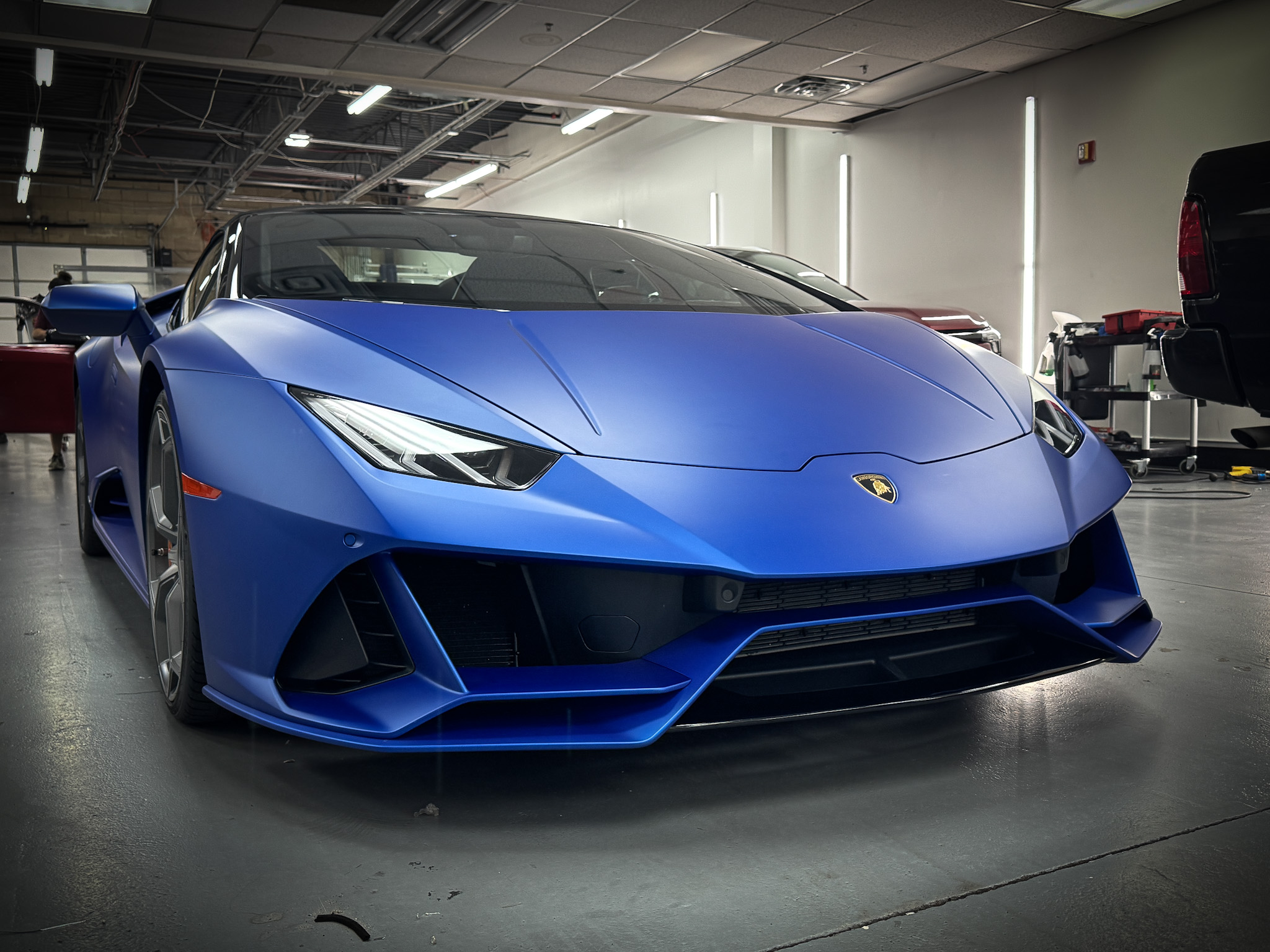 Blue sports car with sharp angles and sleek design inside a garage, with lighting reflecting off its surface.