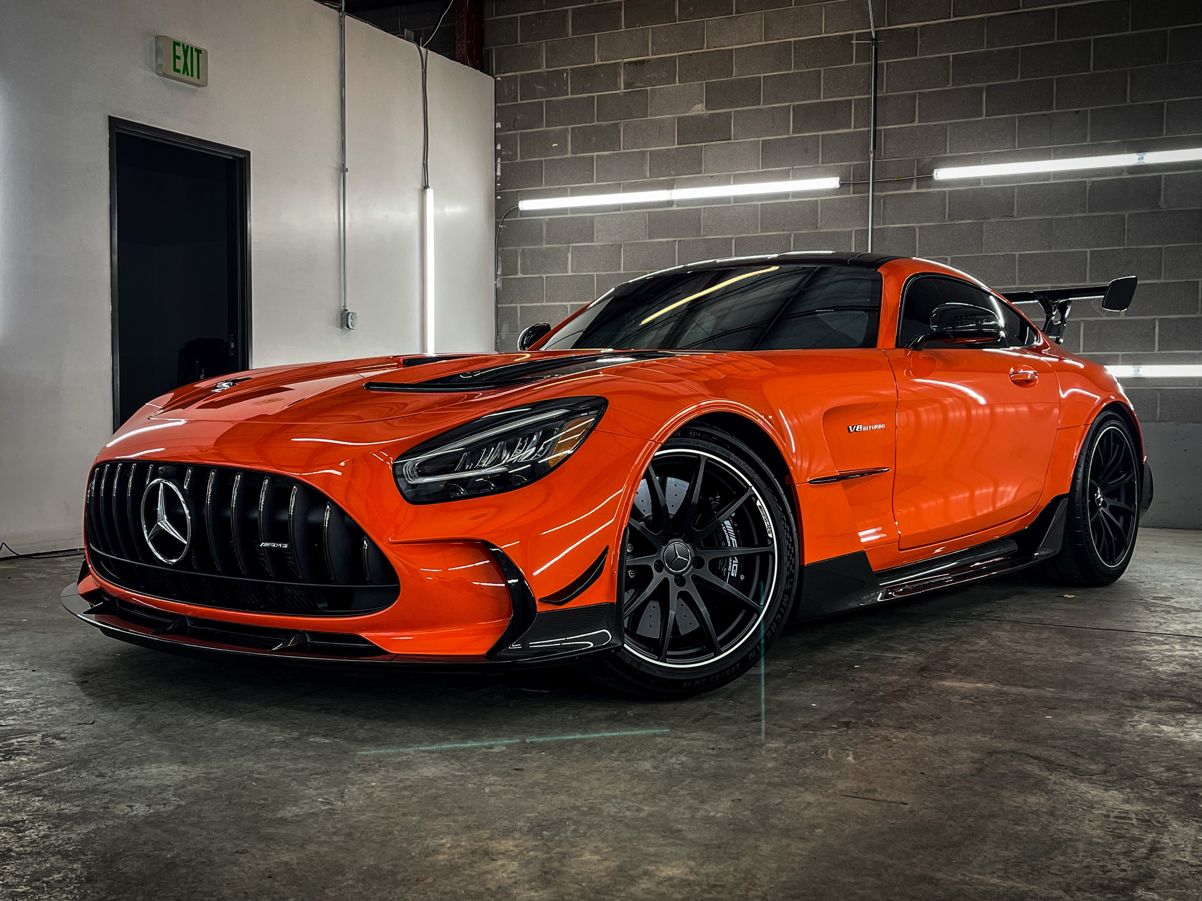 Orange Mercedes-Benz sports car with black accents parked indoors against a brick wall and concrete floor.