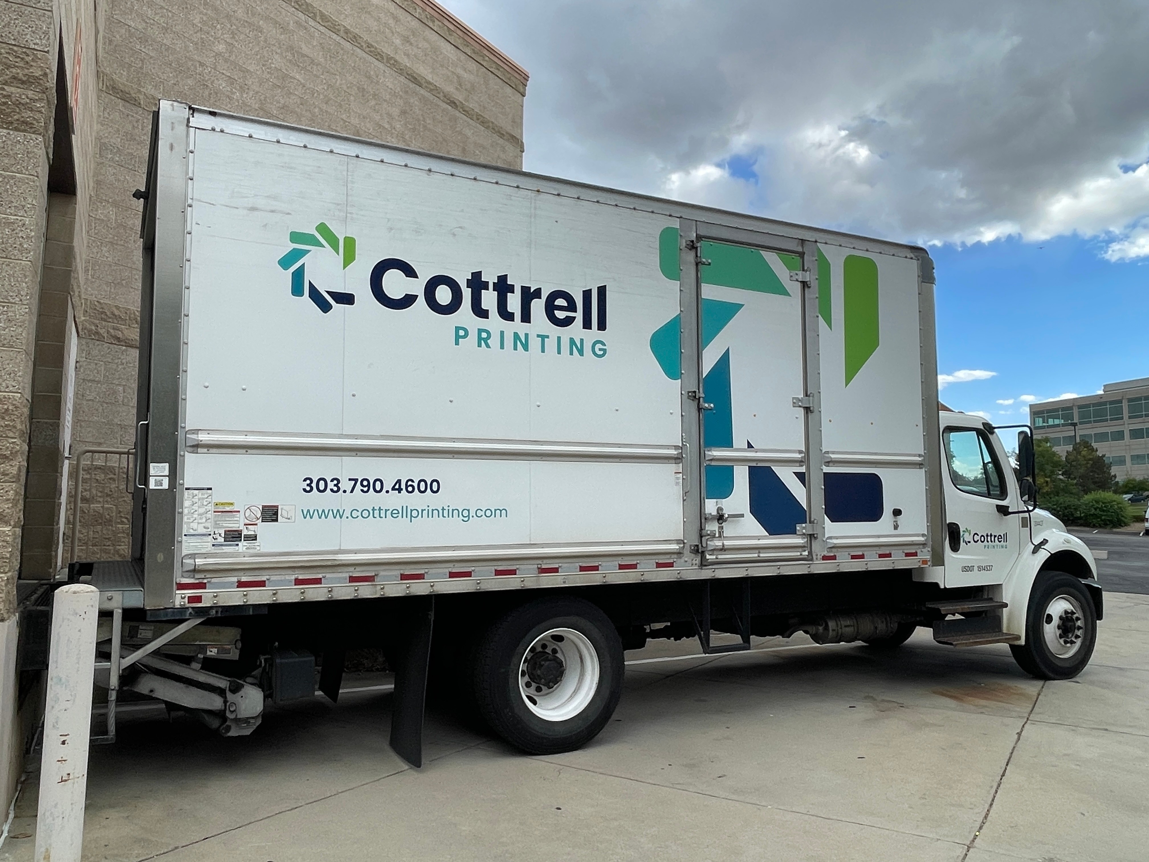 Delivery truck with Cottrell Printing logo parked outside on a concrete surface under cloudy sky.