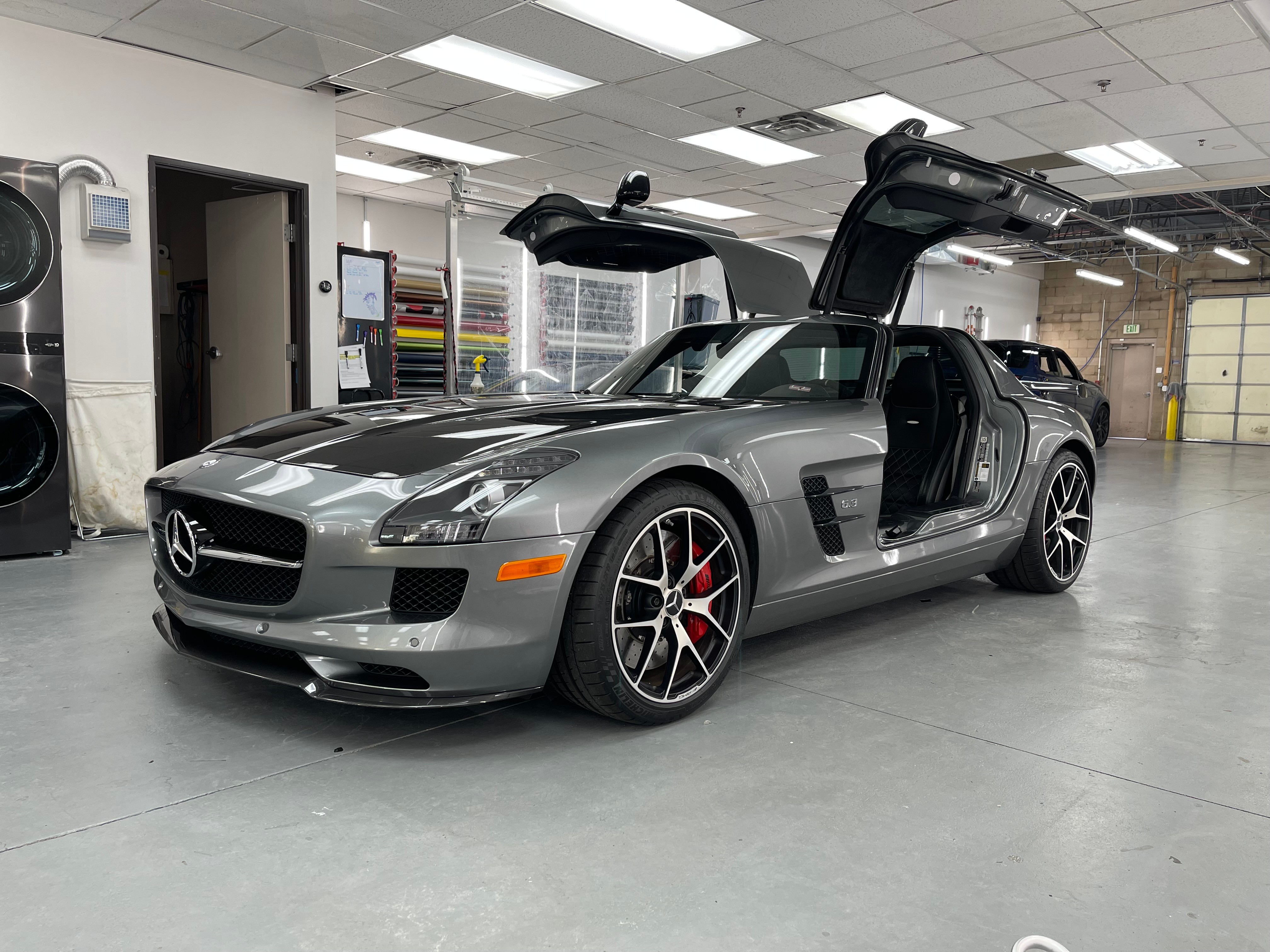 Silver Mercedes-Benz SLS AMG with gullwing doors open inside a garage, showing the car's front and side view.