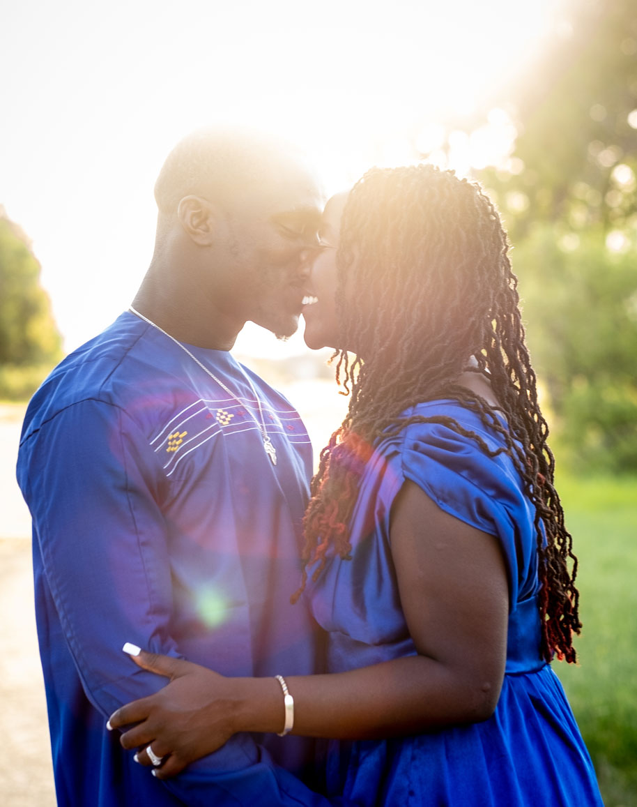 Two people face each other outdoors, with sunlight behind them, embracing and holding hands, wearing blue clothing.