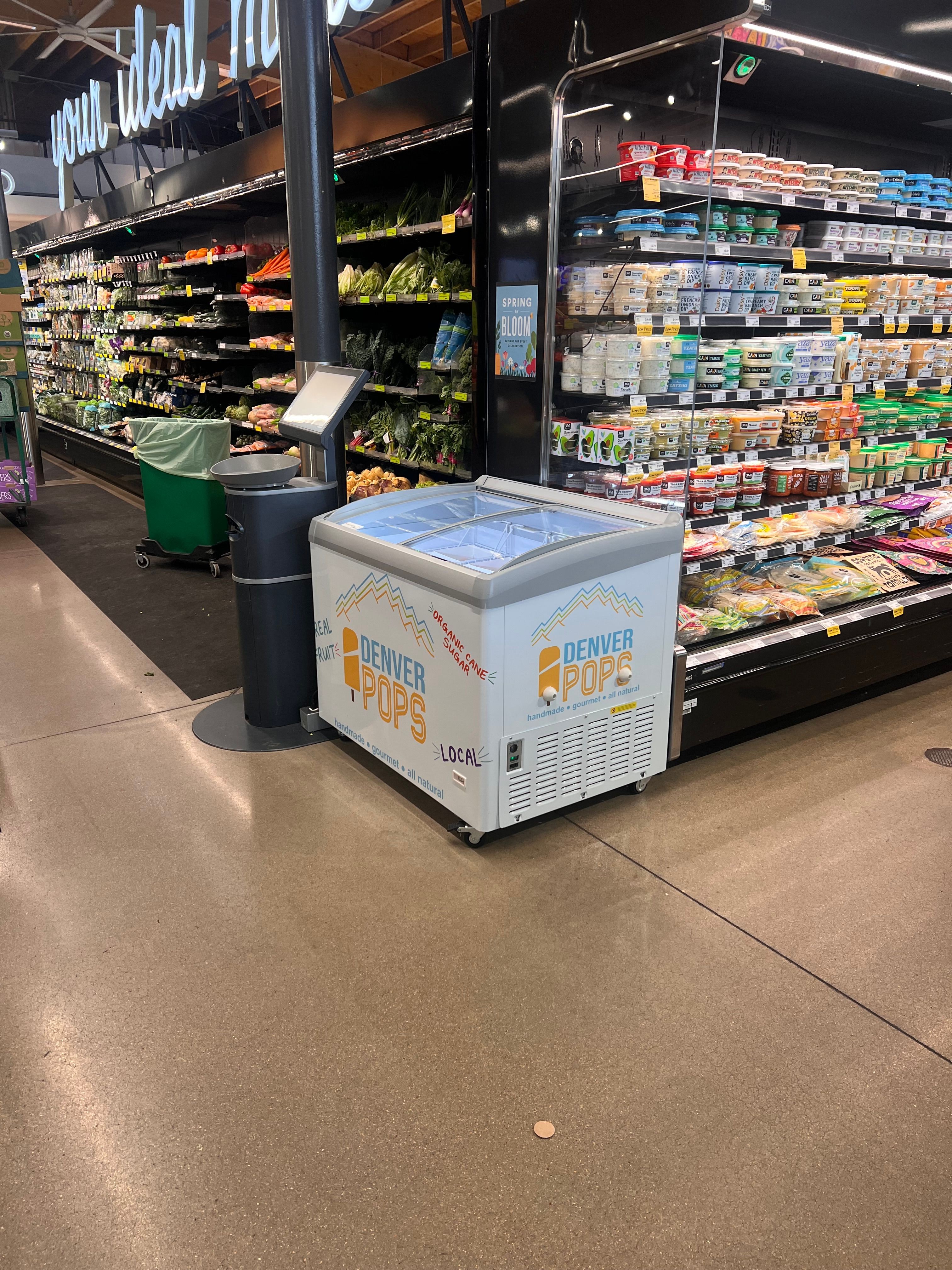Grocery store aisle with refrigerated section, shopping cart, and a box on the floor.