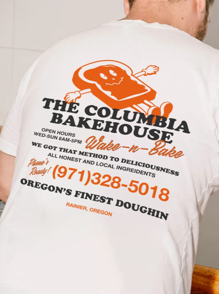 Back of a person wearing a white T-shirt with a logo of a gingerbread man and text about a bakery, Oregon's doughnut shop.